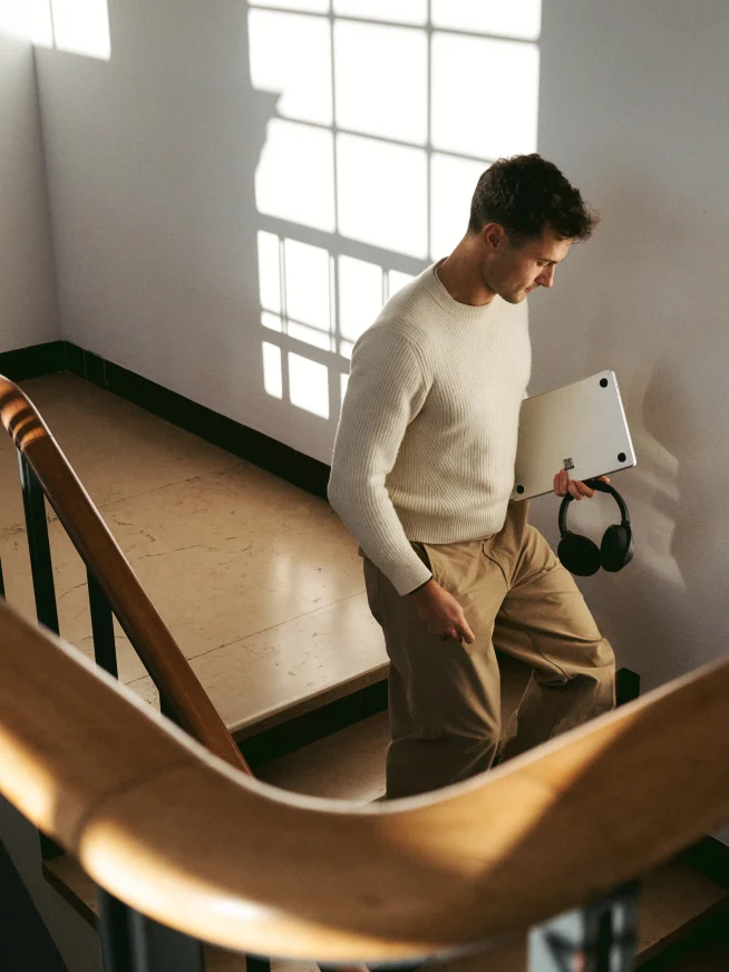 man walking down the stairs with a laptop and headphones in his hand