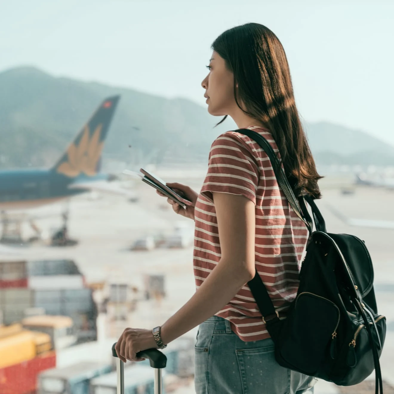 A traveler with a backpack at an airport, holding a phone, near an aircraft, with payment processing by Adyen visible.