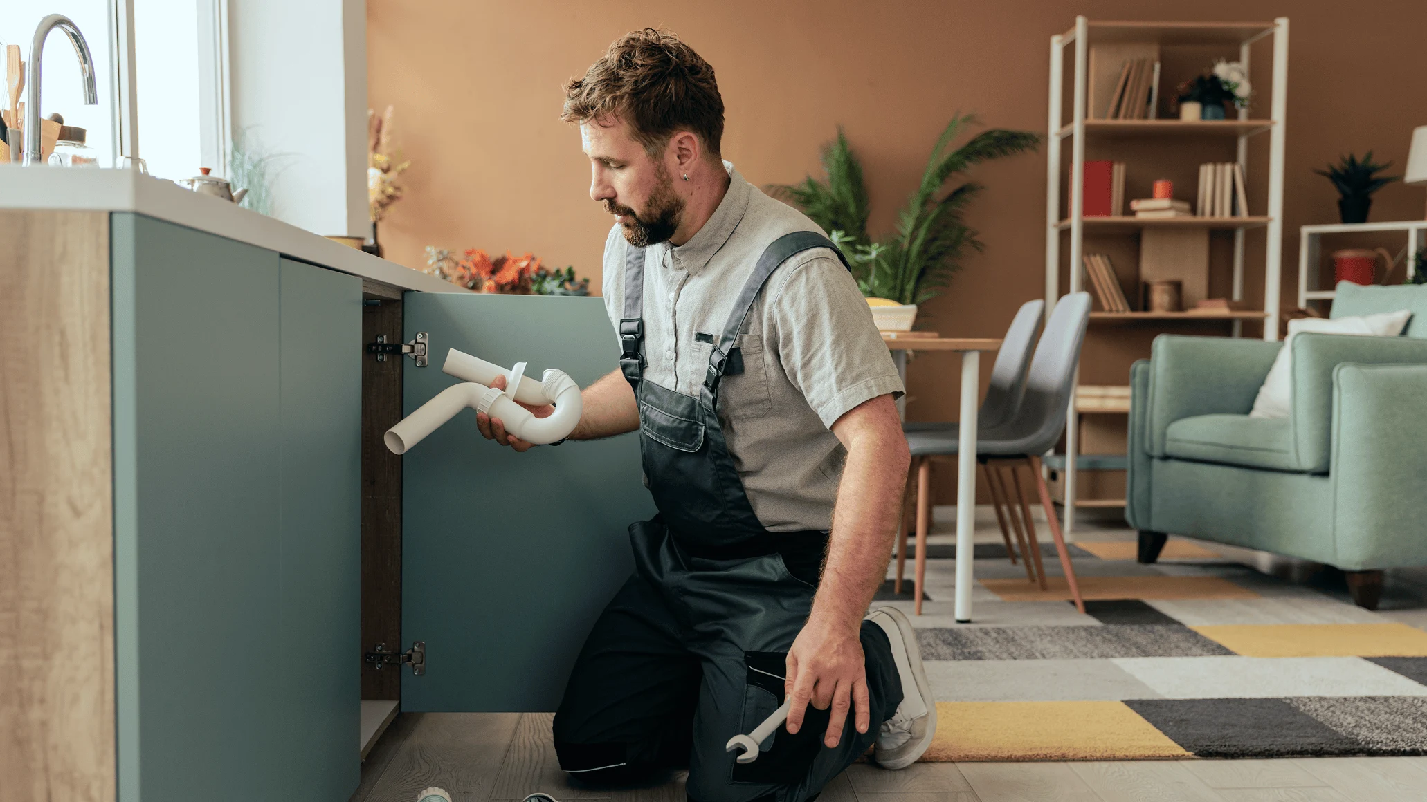 A person kneeling by a kitchen cabinet with a flashlight, possibly inspecting or repairing it.