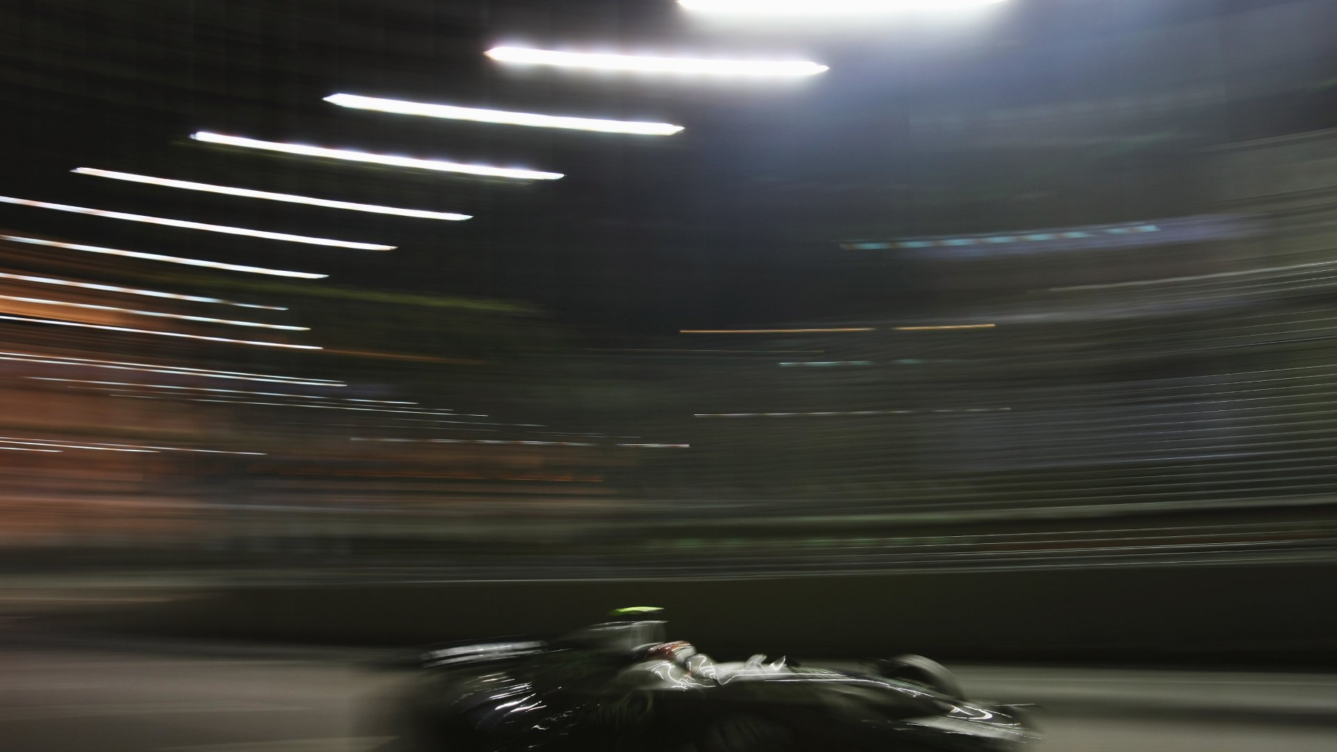A race car speeding along a circuit at night under floodlights, highlighting advanced motorsport engineering.