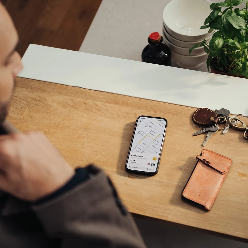 A person holds a smartphone displaying a map, with keys, a wallet, and plant nearby