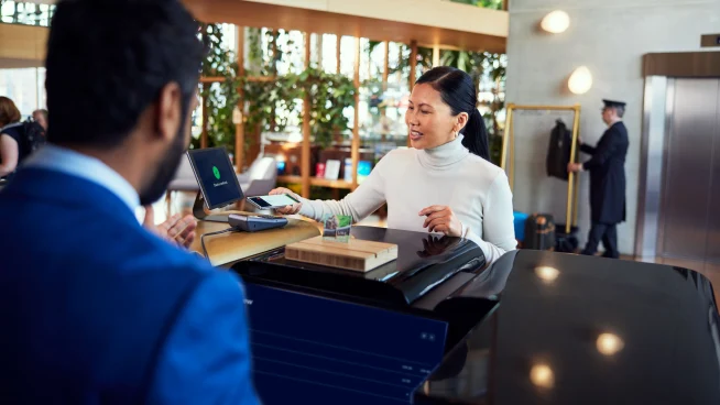 A woman at a hotel reception desk paying by tapping her smartphone at Adyen's terminal.