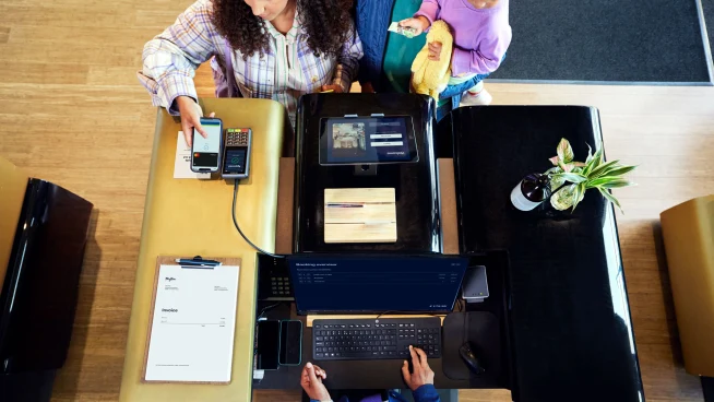 A family at a hotel reception desk making a payment by tapping a smartphone at Adyen's P400 Plus terminal.