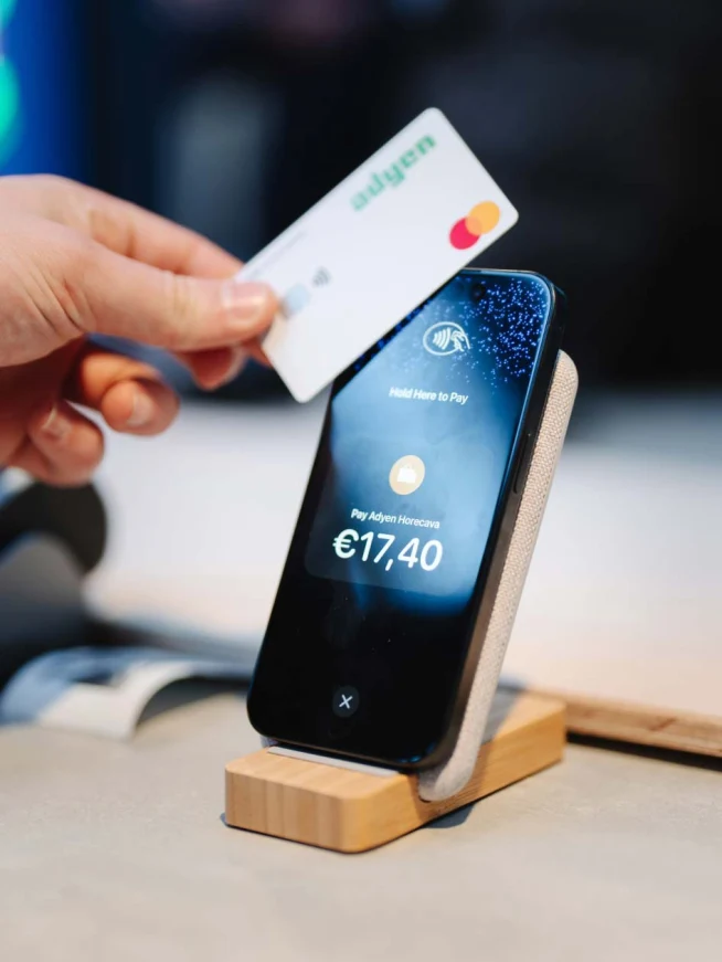 Hand houdt een Adyen-betalingkaart bij een smartphone met een betalingstotaal van €17,40.