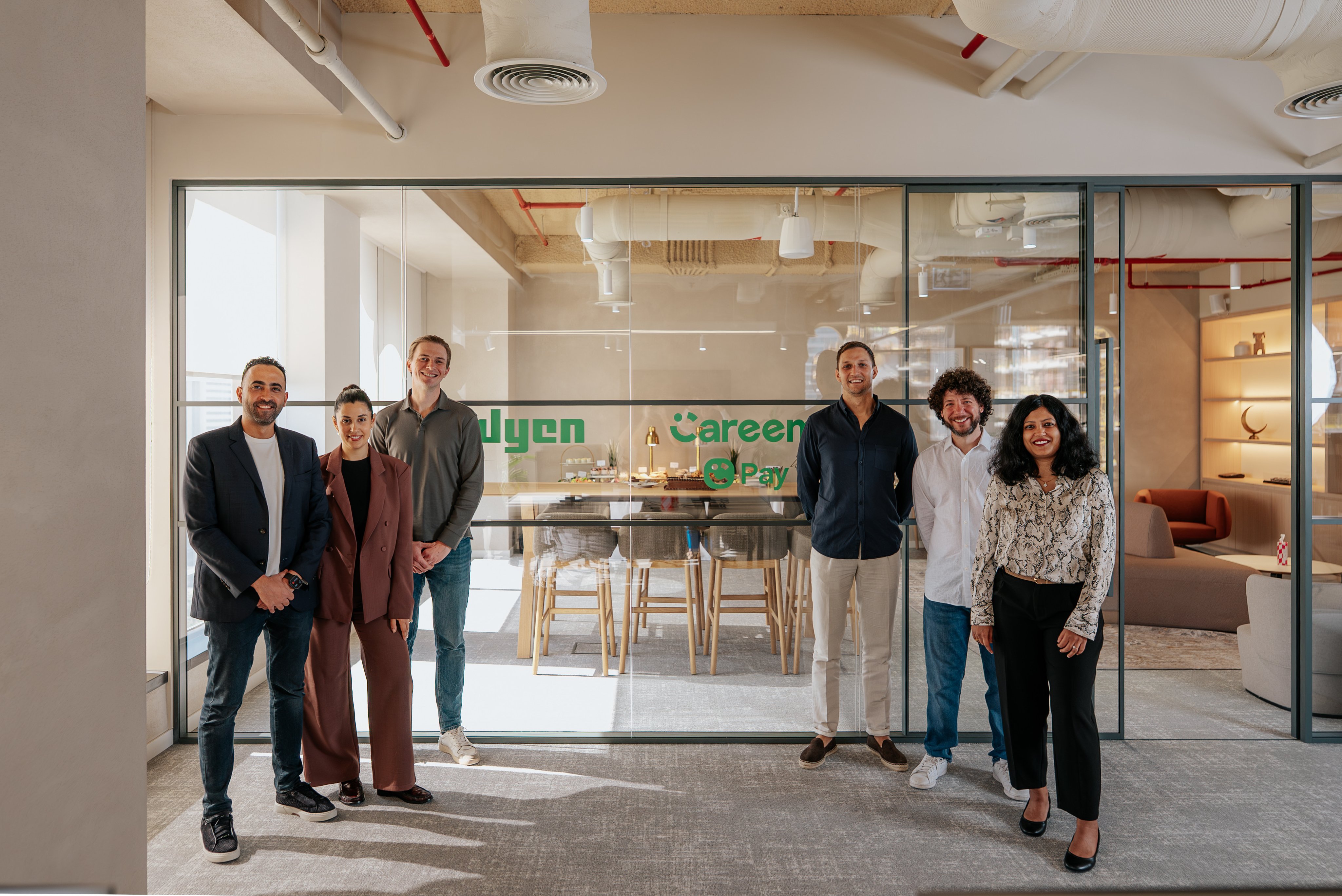 Adyen team members standing inside the Adyen office in front of a glass wall.