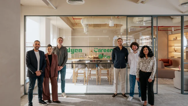 Adyen team members standing inside the Adyen office in front of a glass wall.
