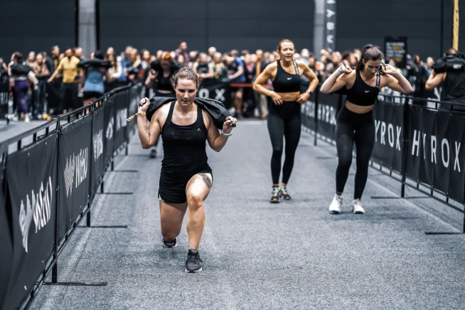 Women crossing finish line after a race at a sporting event, with race barriers in the background