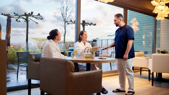 Two women at a table paying for spa and wellness by tapping their card at Adyen's S1E terminal.