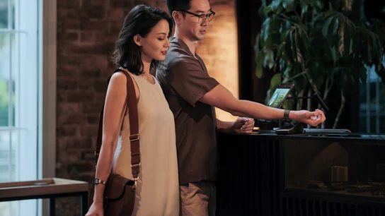 A couple self-checking into a hotel room at reception and paying for their stay by tapping a smartwatch on Adyen's terminal.