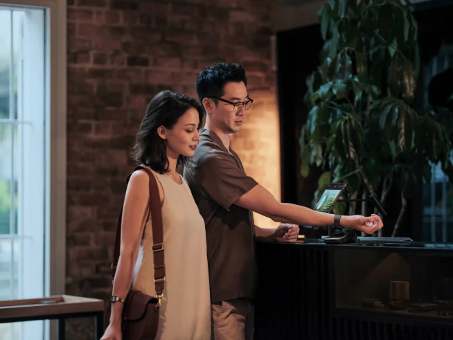 A couple self-checking into a hotel room at reception and paying for their stay by tapping a smartwatch on Adyen's terminal.
