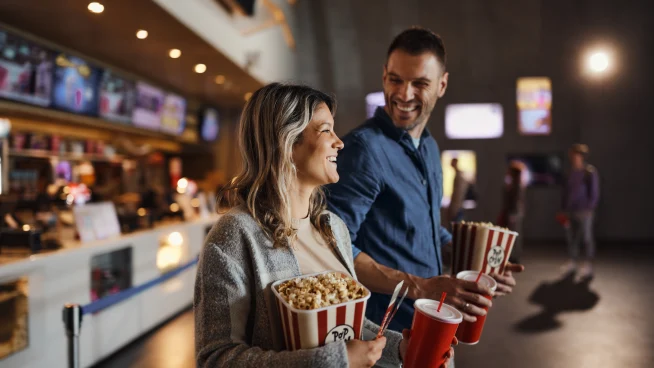A couple enjoying popcorn and drinks at a cinema, with payment by Adyen.