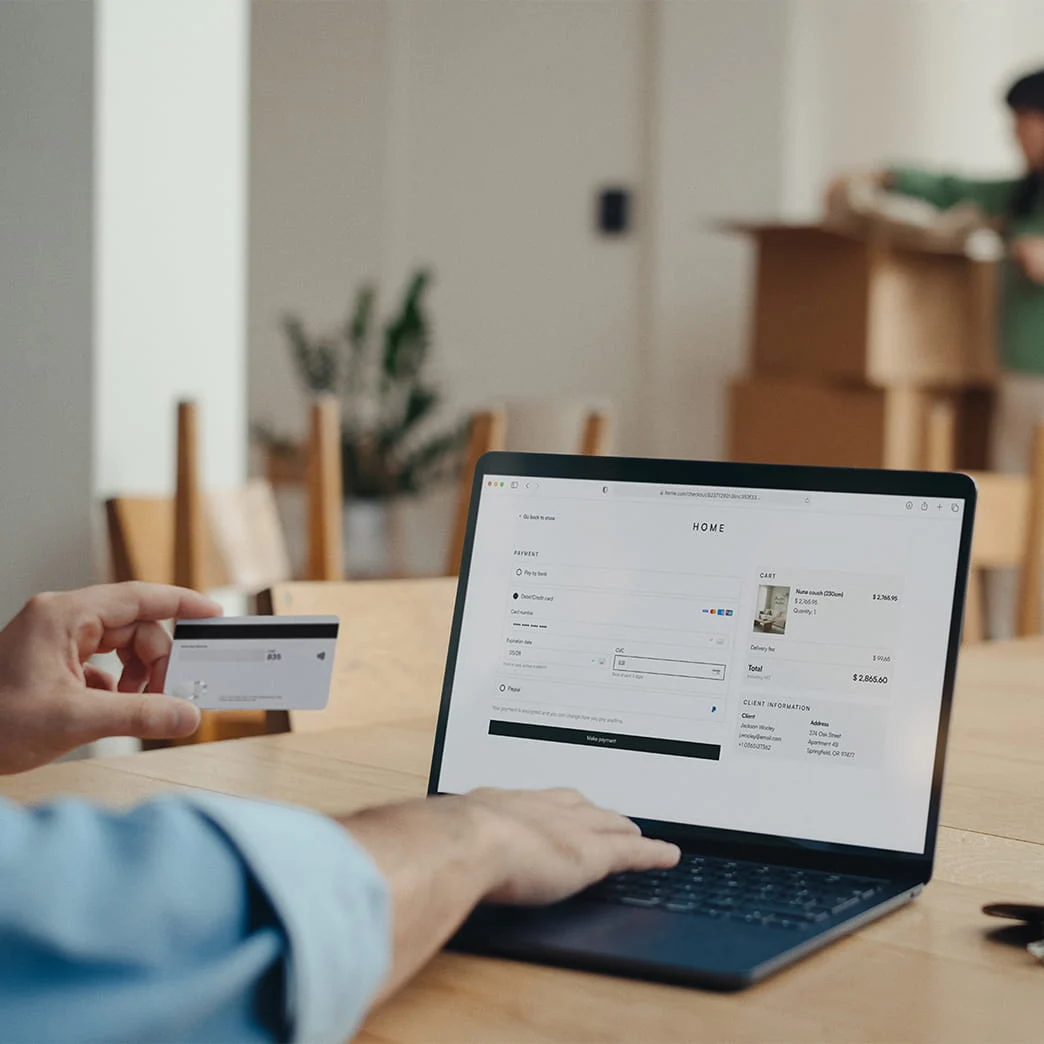 A person making an online payment on a laptop with an Adyen terminal visible in the background