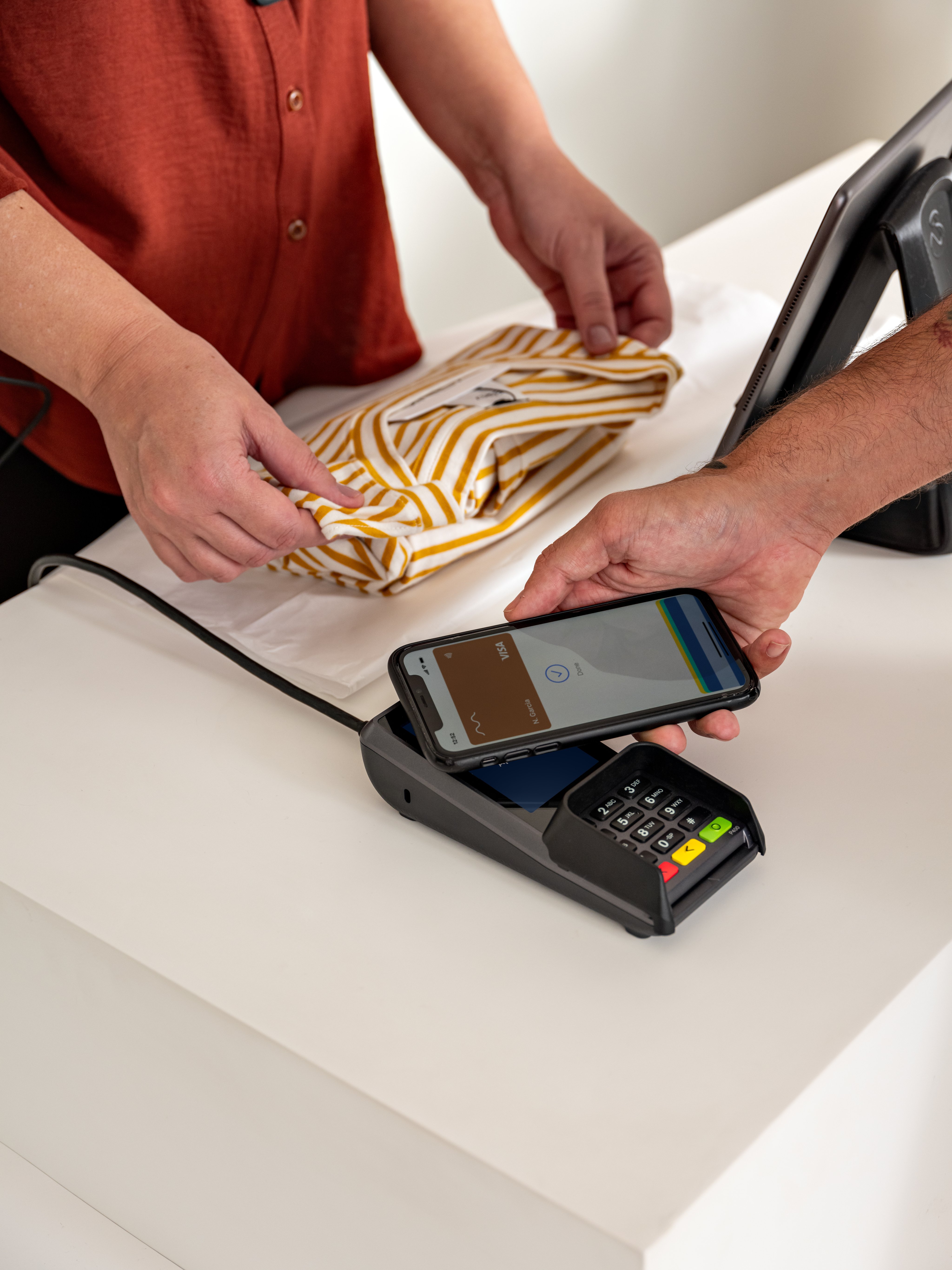 A customer in a fashion store paying by tapping their phone at Adyen's P400 Plus terminal.
