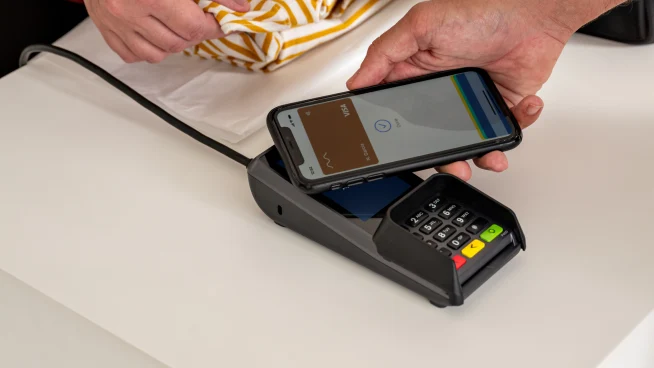 Un cliente in un negozio di moda paga toccando il telefono sul terminale Adyen P400 Plus.
