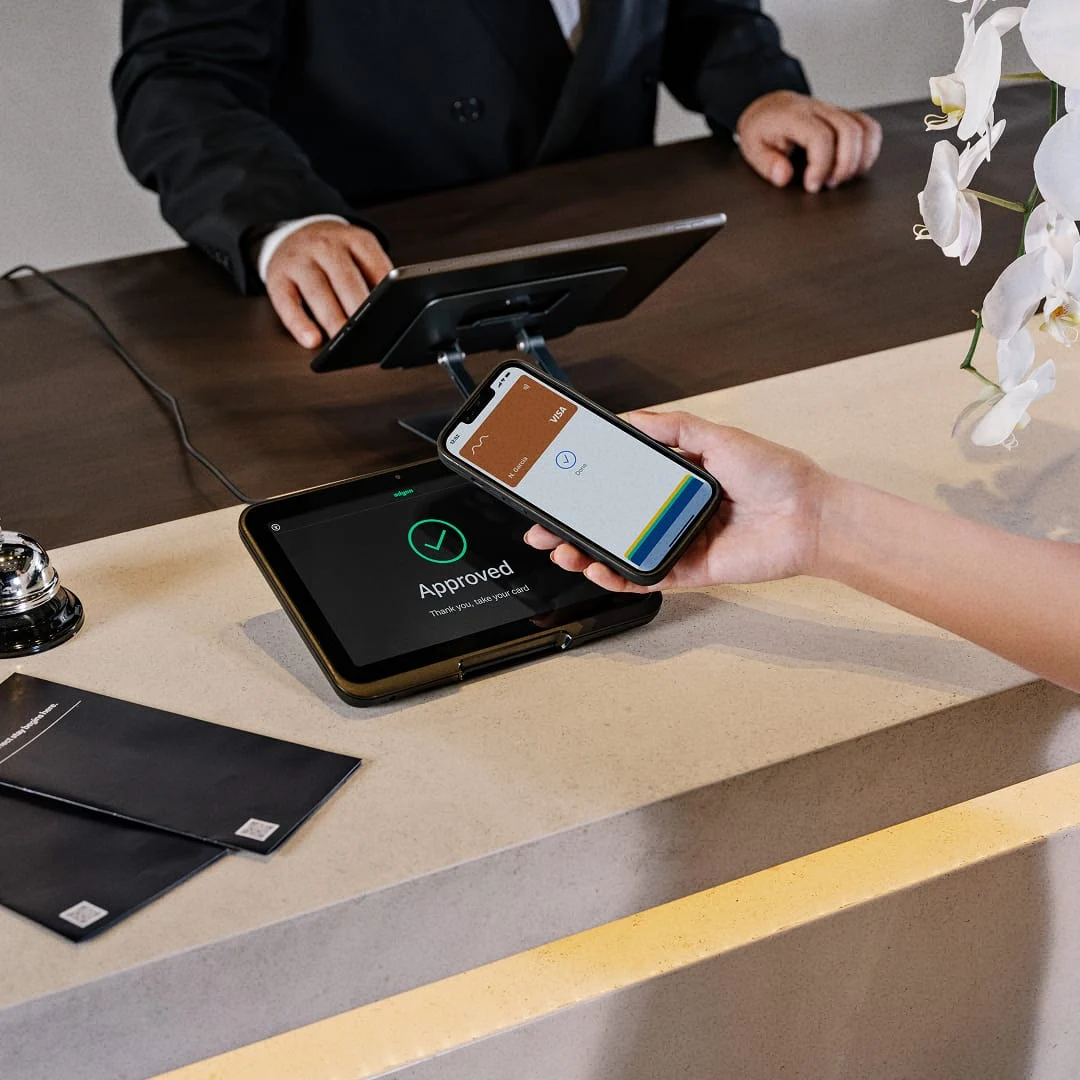 A customer pays with a smartphone at an Adyen card terminal, approved payment visible, in a business setting.