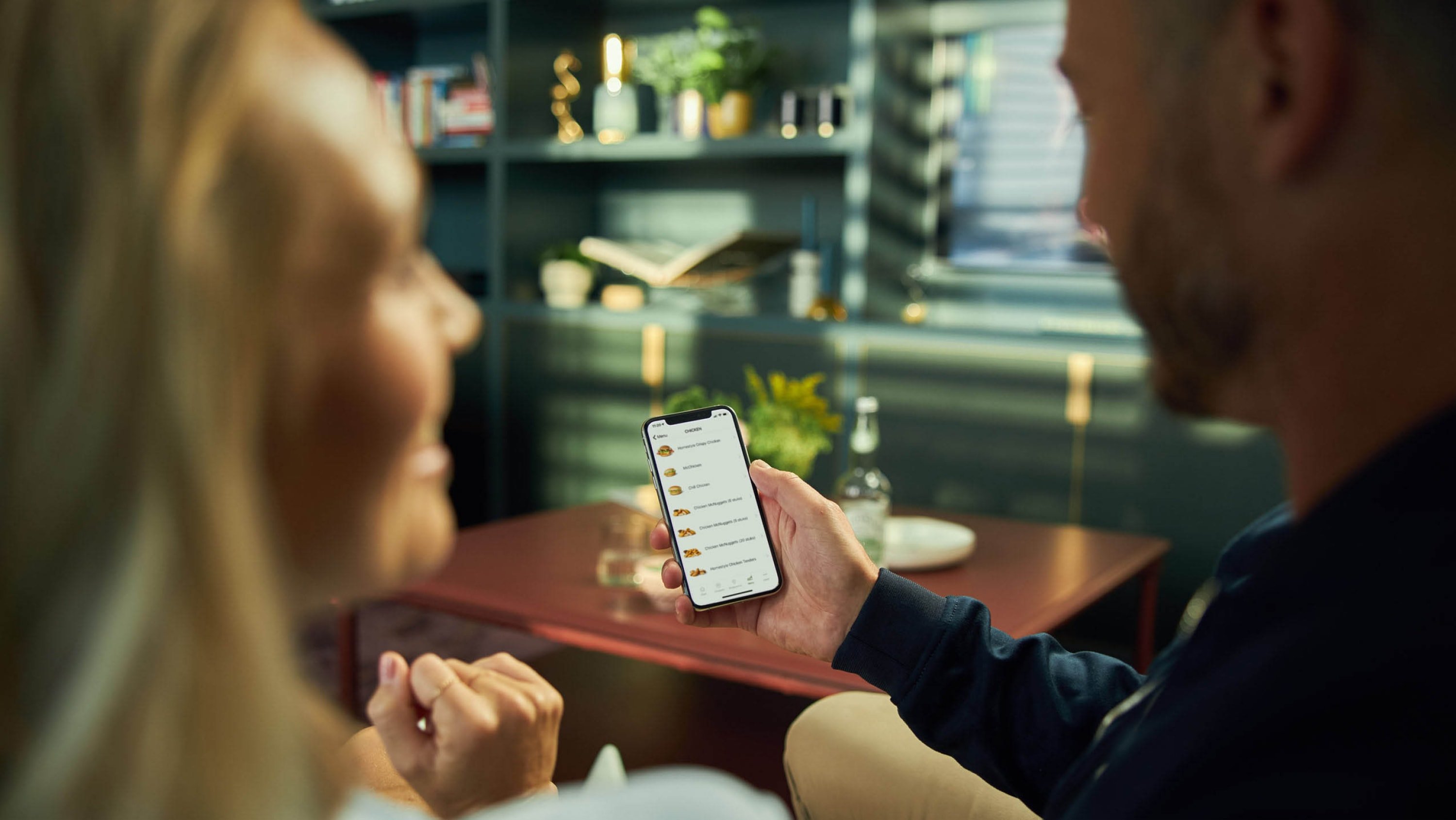 Zwei Personen betrachten eine mobile Zahlungs-App beim Abendessen in einer gemütlichen Atmosphäre.