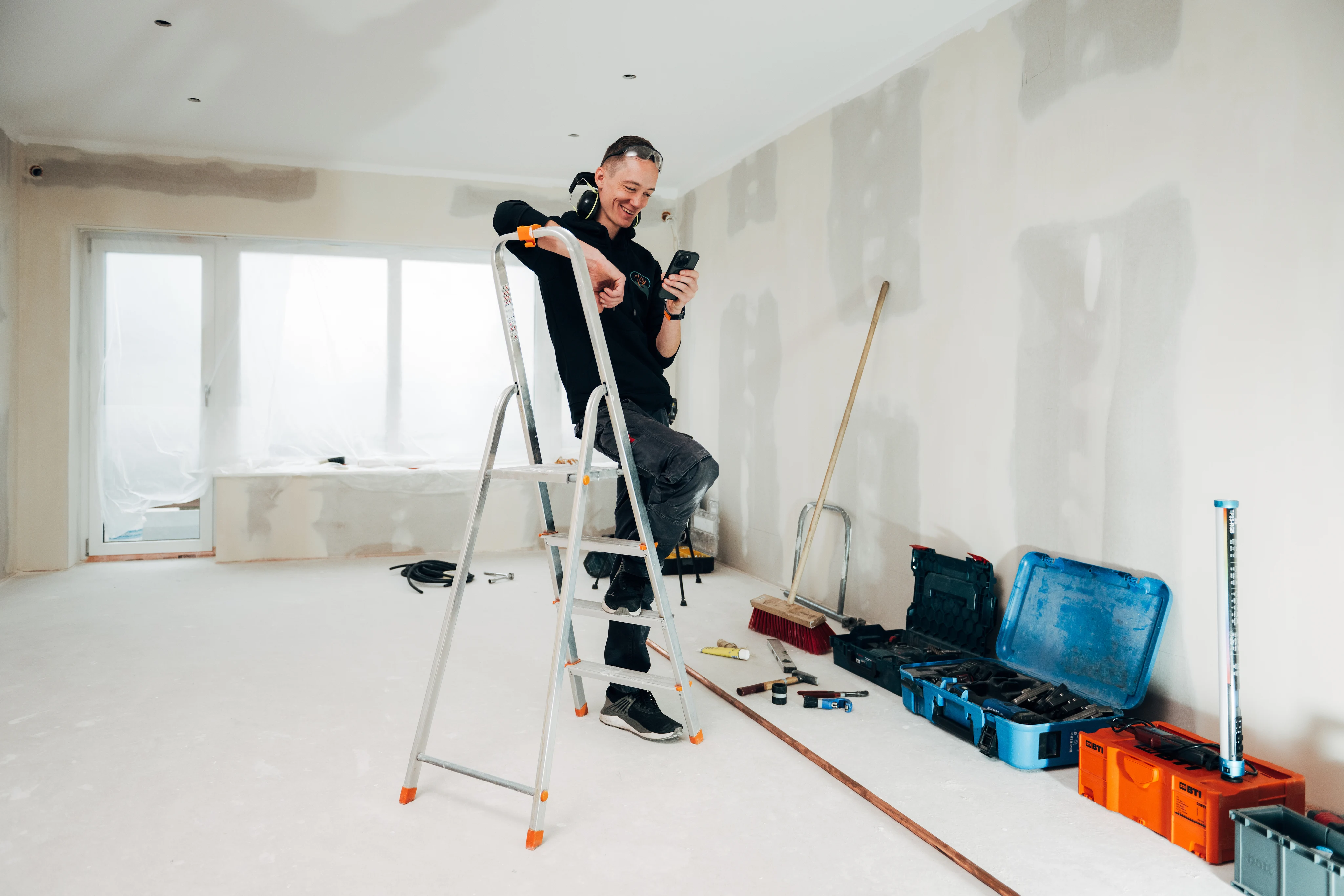 Tooltime employee on a ladder checking his mobile phone in an empty room.