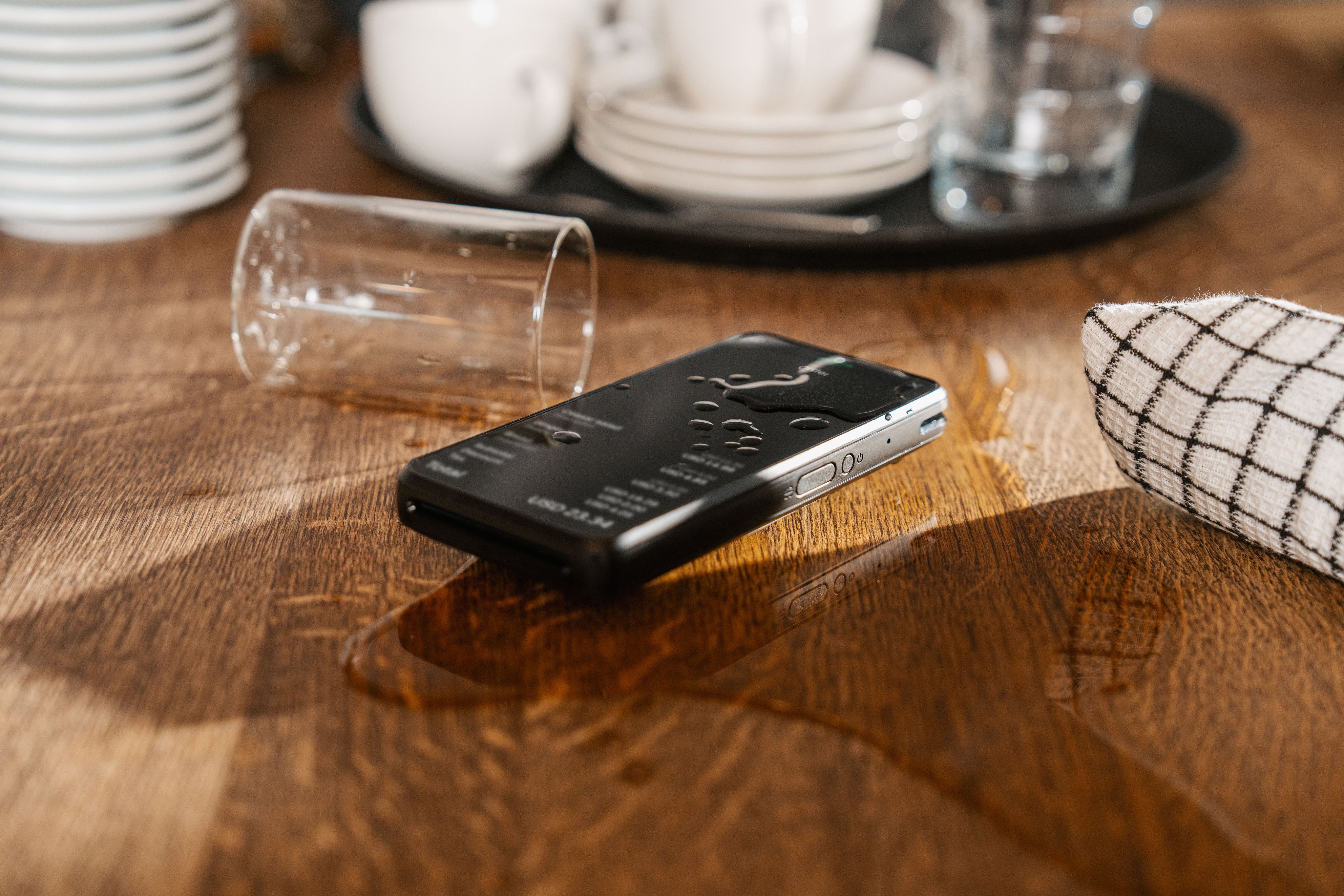 Black smartphone on wooden table near a spilled glass and dishware in a restaurant setting