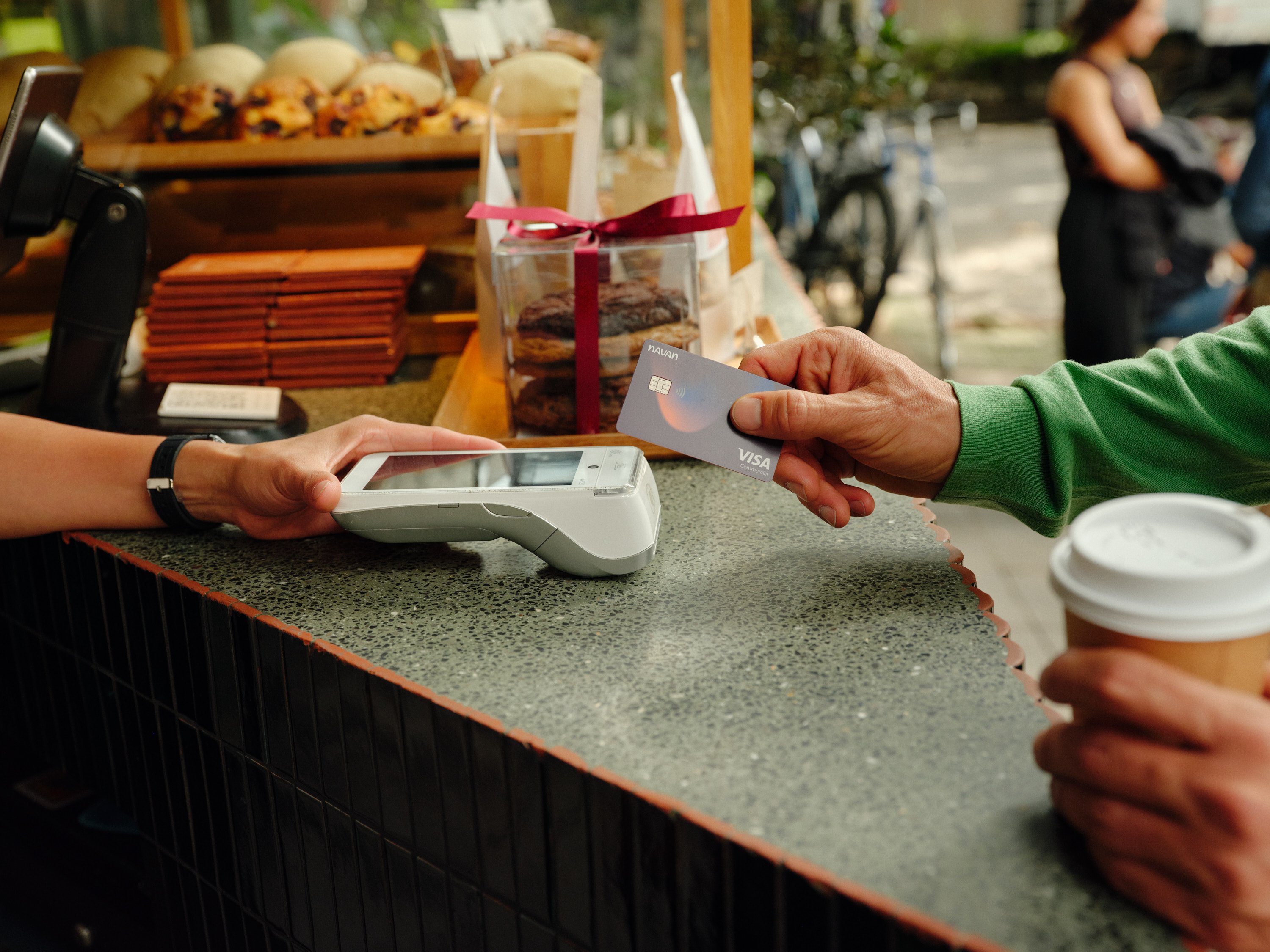 A customer paying with a card at an Adyen payment terminal while holding a coffee outside a cafe.