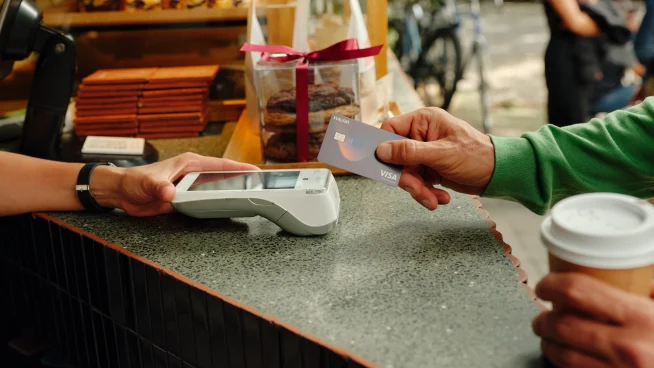 A customer paying with a card at an Adyen payment terminal while holding a coffee outside a cafe.