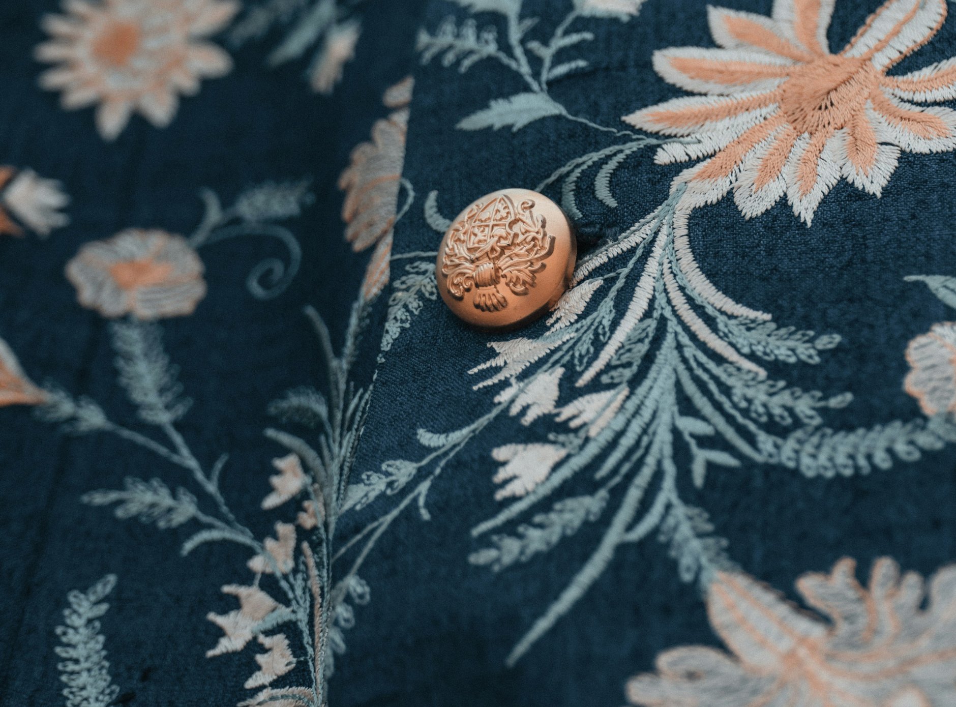 Close-up of a decorative button on embroidered fabric with floral patterns, no visible payment activity.