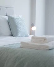 A neatly made bed with pillows and folded towels in a bright, modern bedroom.