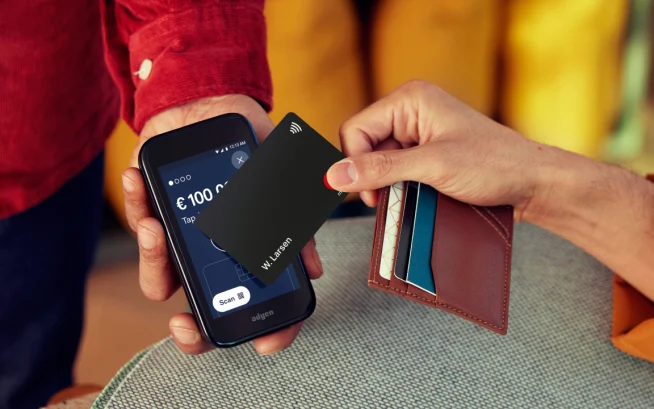 Person tapping a contactless card on a mobile payment terminal displaying the Adyen checkout screen.