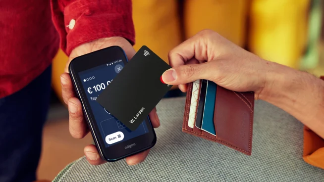 Person tapping a contactless card on a mobile payment terminal displaying the Adyen checkout screen.