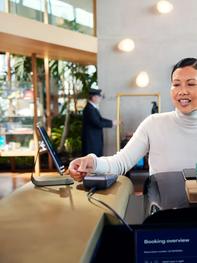 En kvinne ved resepsjonen på et hotell som gjør et betaling ved å tappe et kort på Adyens P400 Plus-terminal.