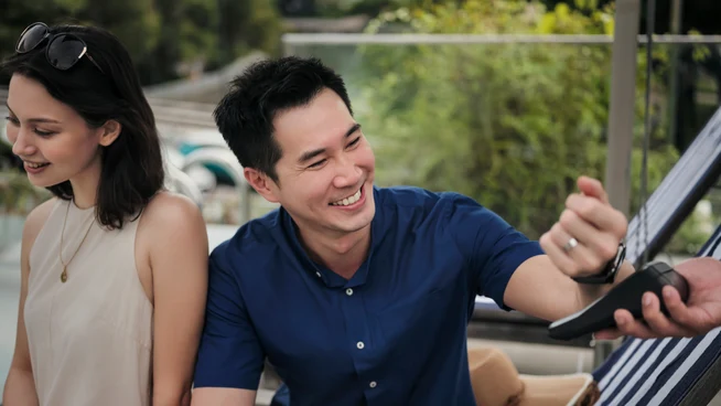 Um casal na piscina de um hotel, pagando bebidas tocando seu smartwatch no terminal da Adyen.