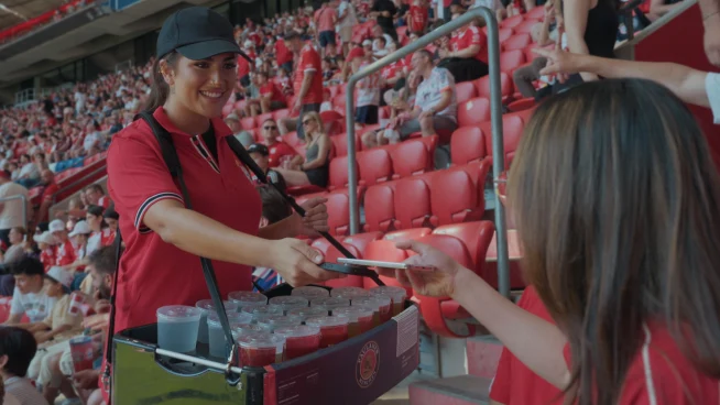 A person purchases drinks from an employee at a stadium concession stand using an Adyen payment terminal.