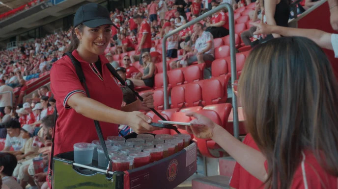 A person purchases drinks from an employee at a stadium concession stand using an Adyen payment terminal.