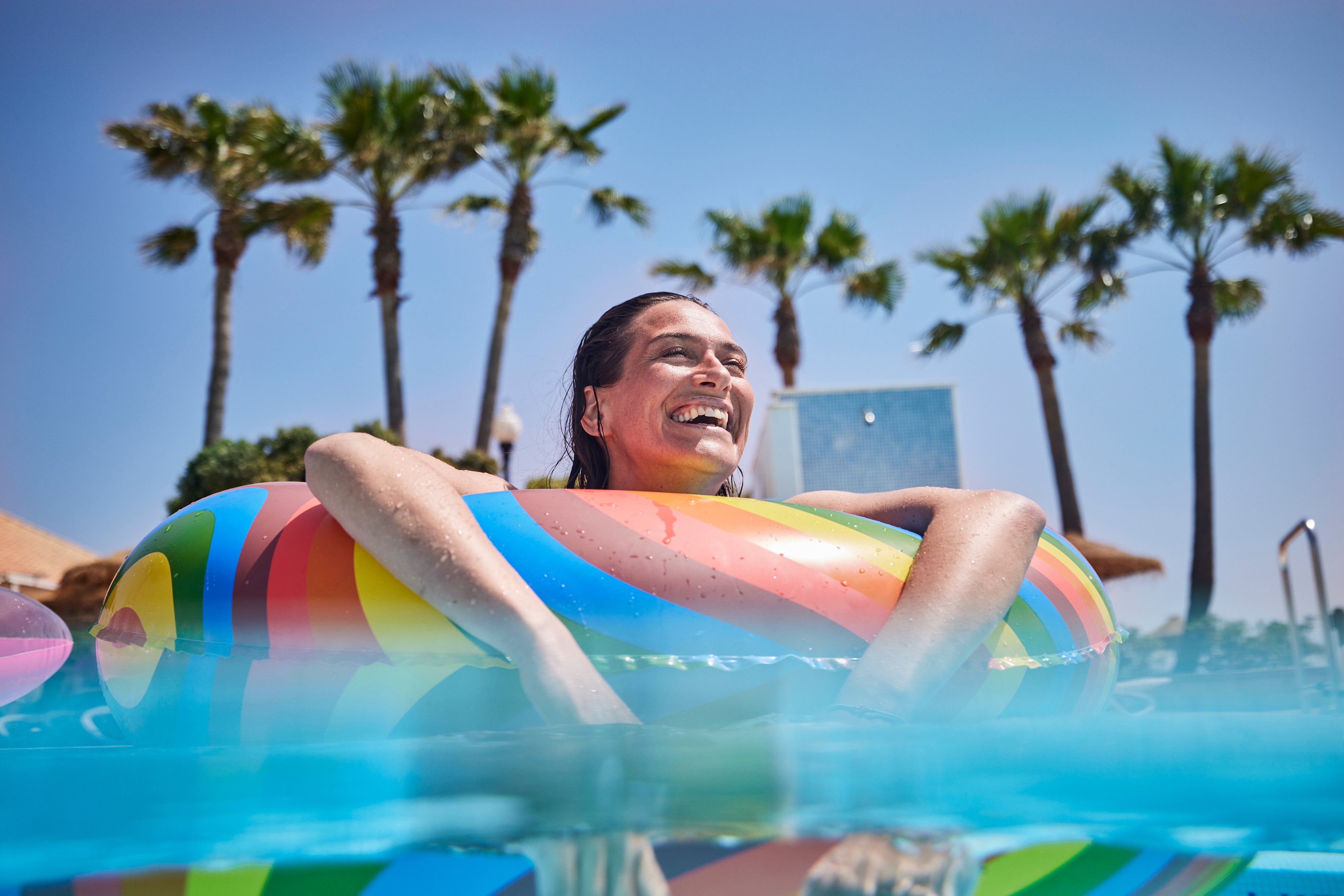 Person in aufblasbarem Schwimmring am Pool mit Palmen im Hintergrund bei Aldiana Urlaub