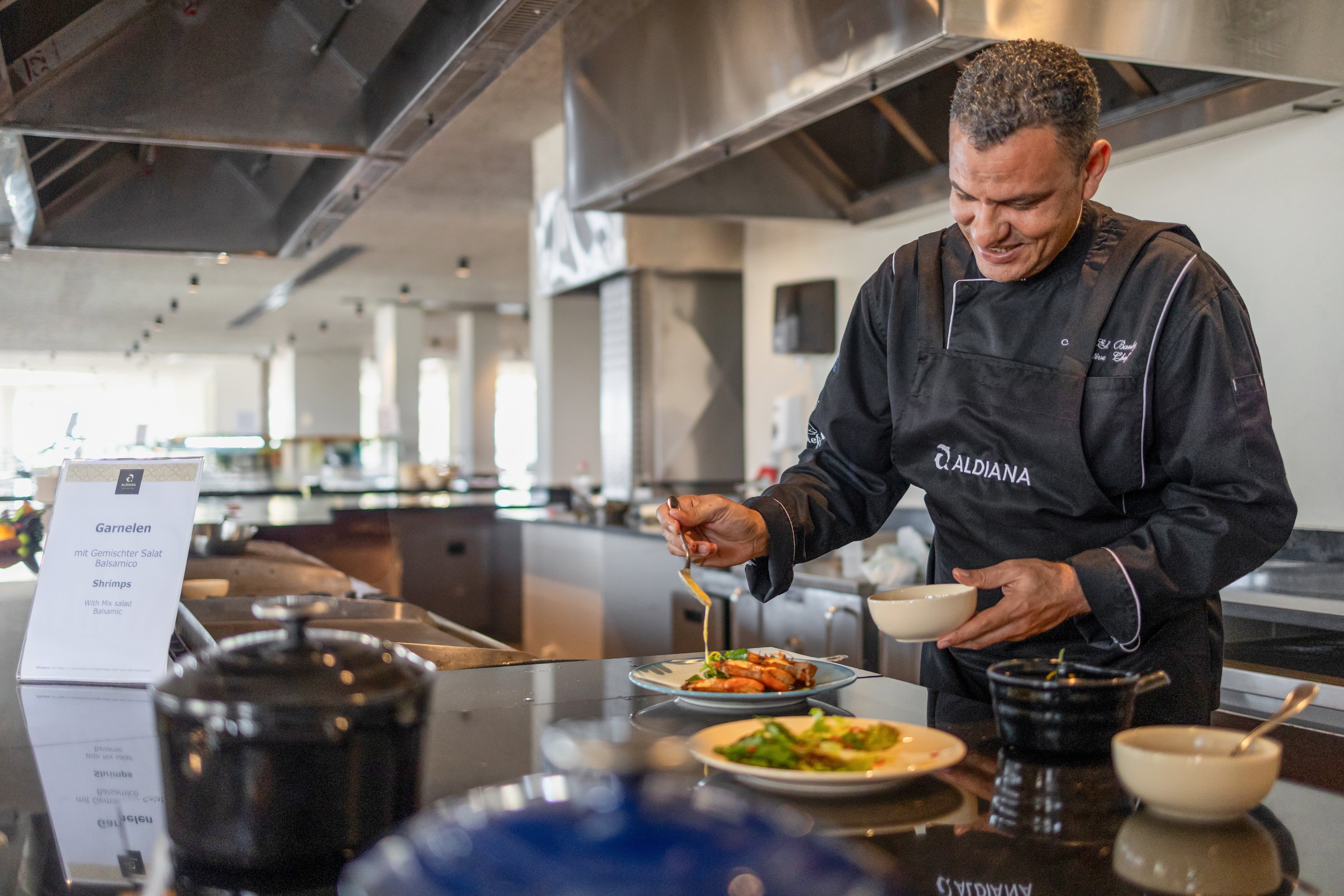 Ein Koch bereitet in einem modernen Küchenbereich im Premium Cluburlaub von Aldiana ein Gericht zu.