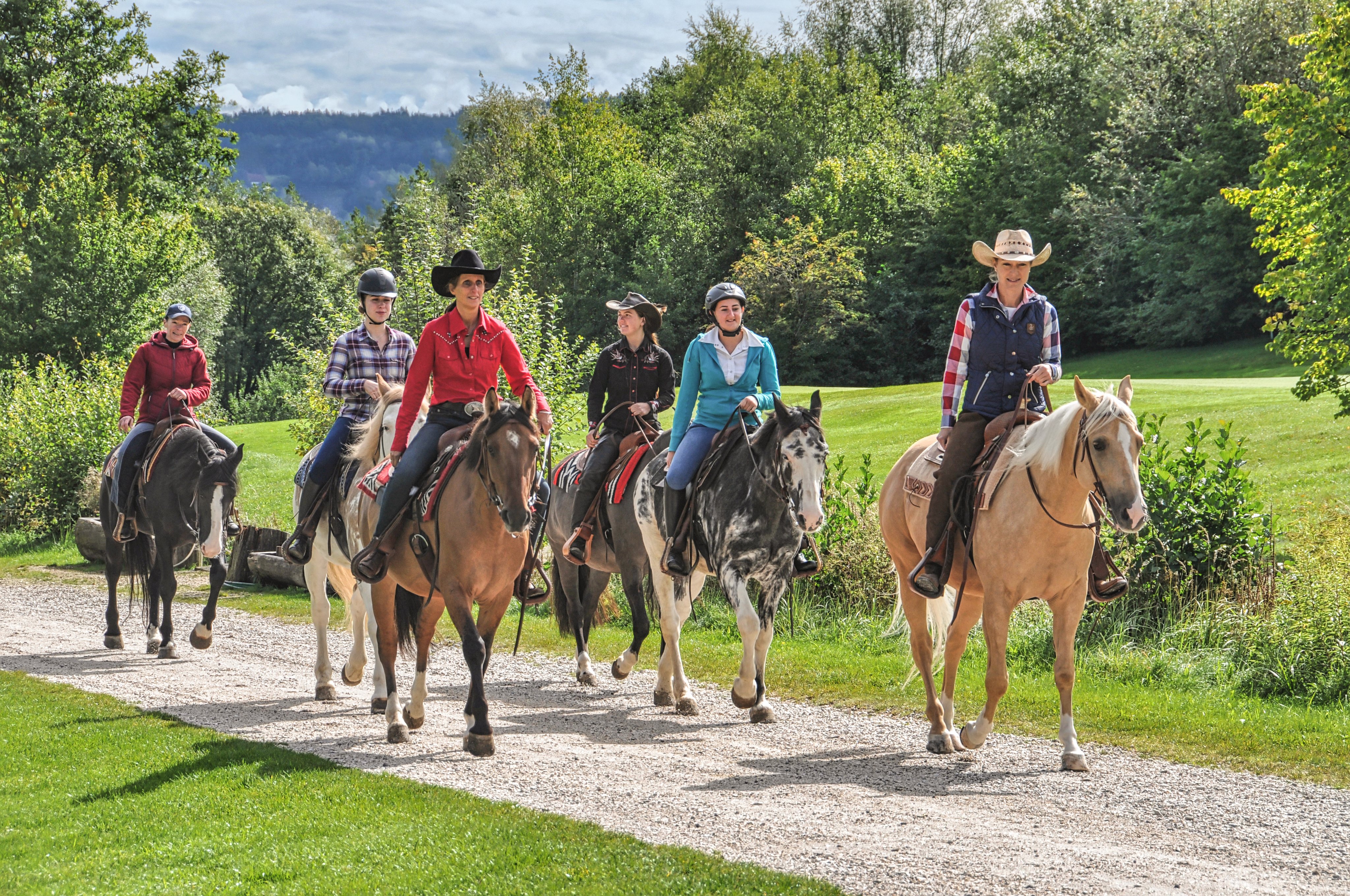 Gruppe von Personen beim Reiten auf einem Reitweg in einer grünen Landschaft
