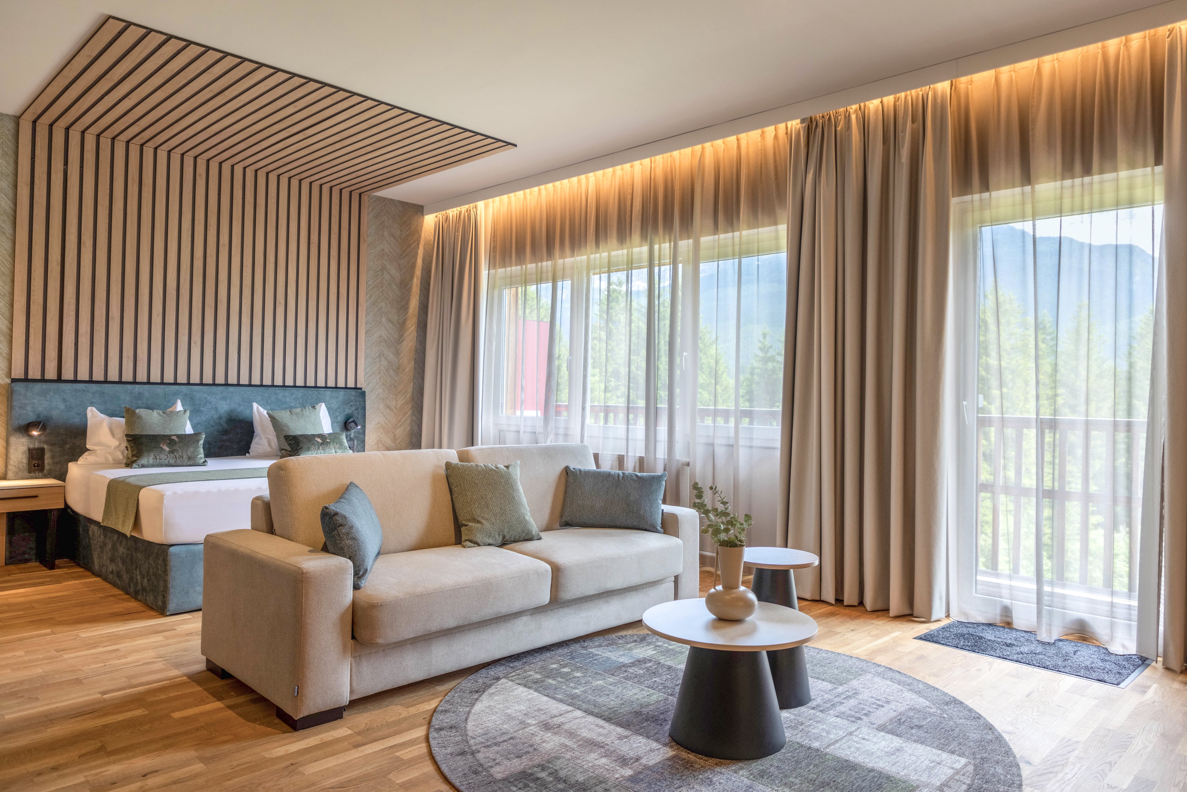 Helles Hotelzimmer mit gemütlichem Sofa, großen Fenstern und Blick auf Berge