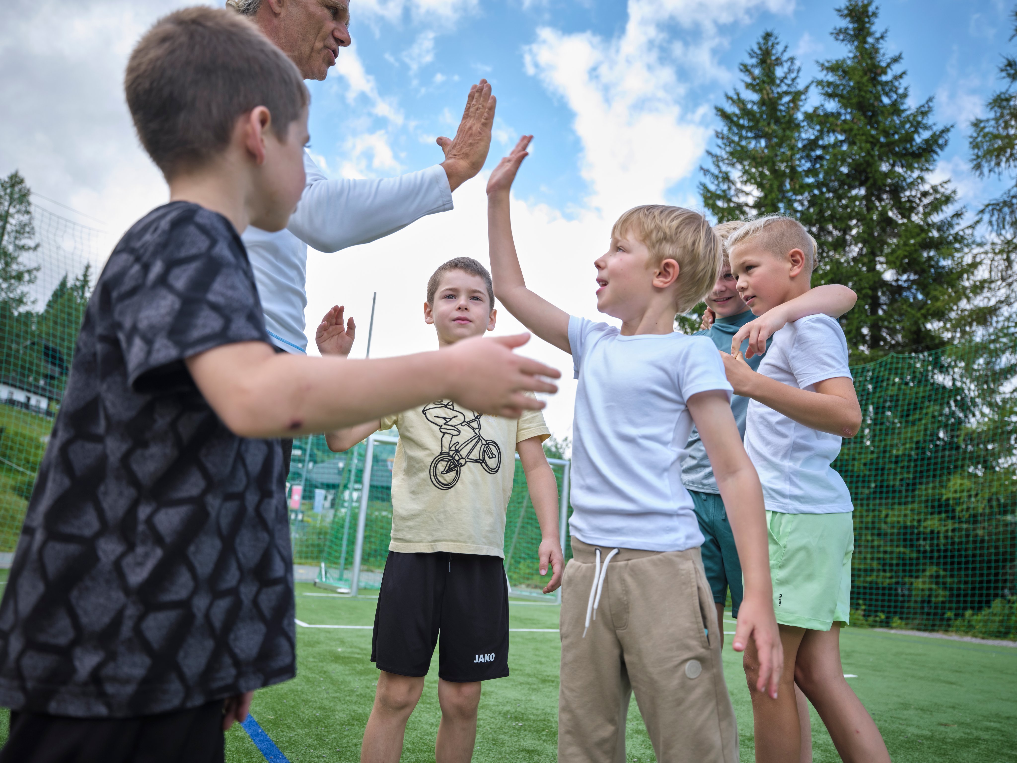 Gruppe von Kindern beim High-Five auf grünem Rasen im Freien bei Sonnenschein