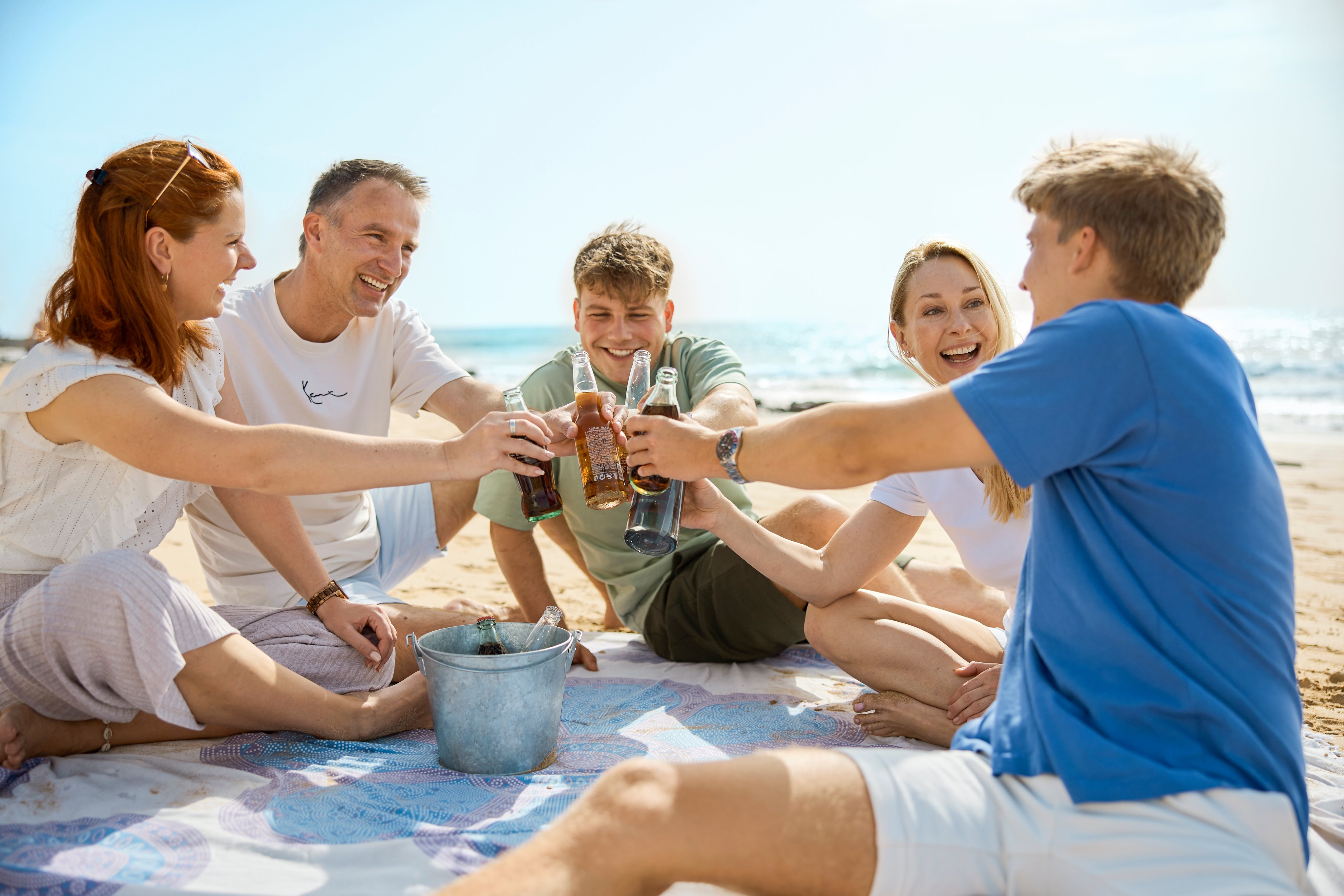 Gruppen von jungen Menschen sitzen am Strand im Kreis und stoßen mit Getränken an