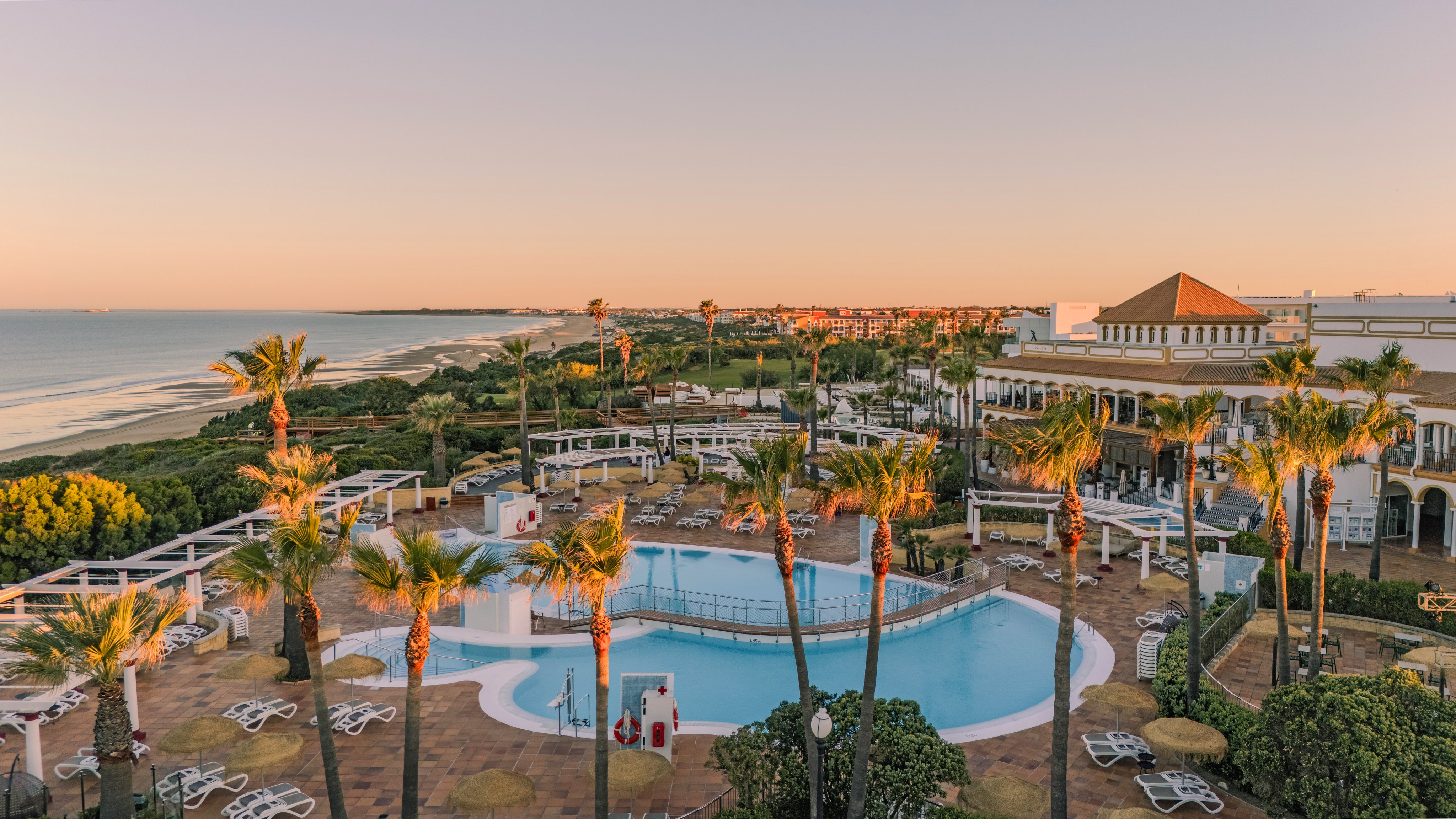 Blick auf den Poolbereich mit Palmen und Meer, Sonnenuntergang, Premium Cluburlaub bei Aldiana