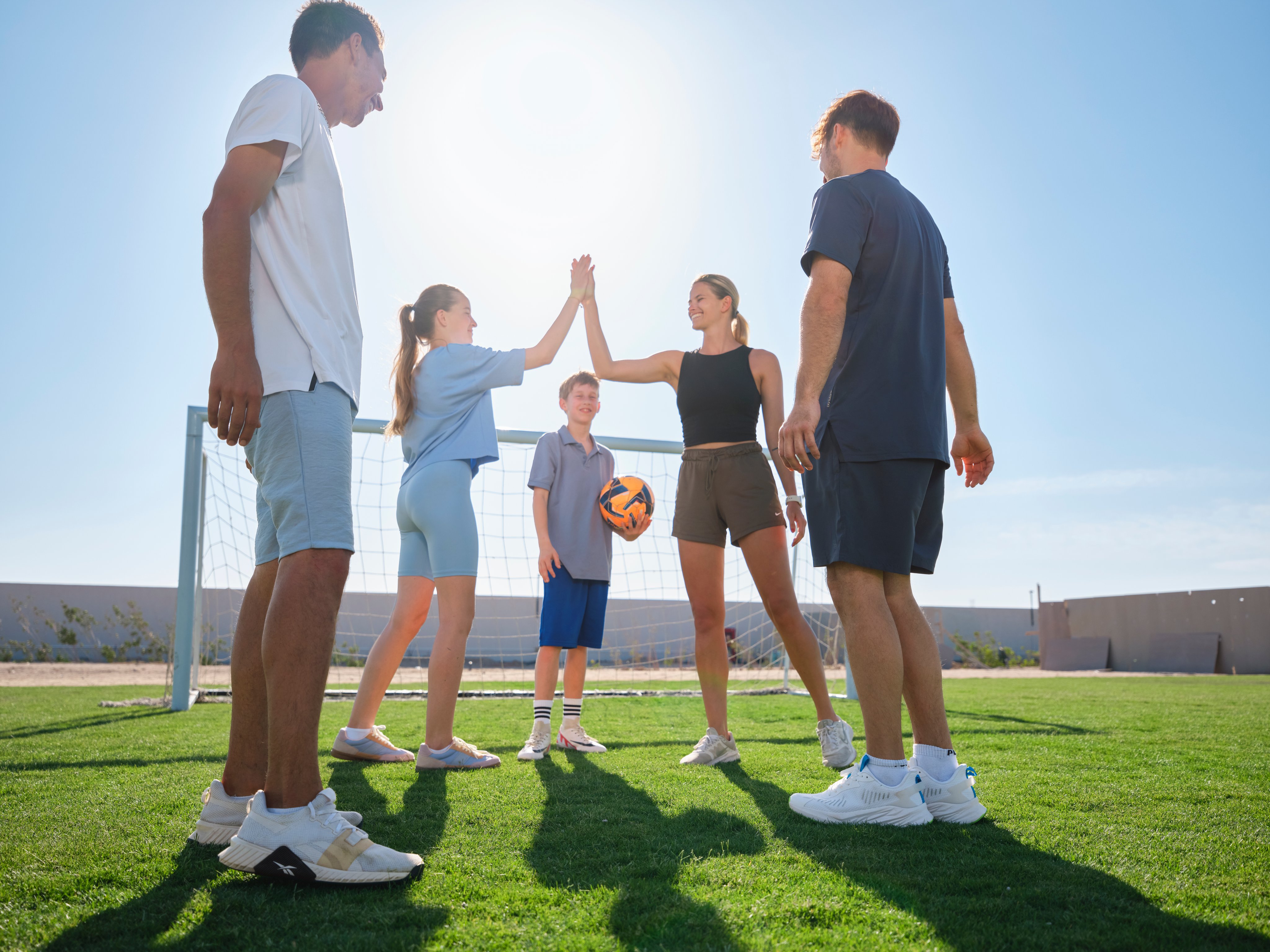 Männer und Frauen beim High-Five auf einem Sportplatz, sonniger Tag, Spaß und Gemeinschaft