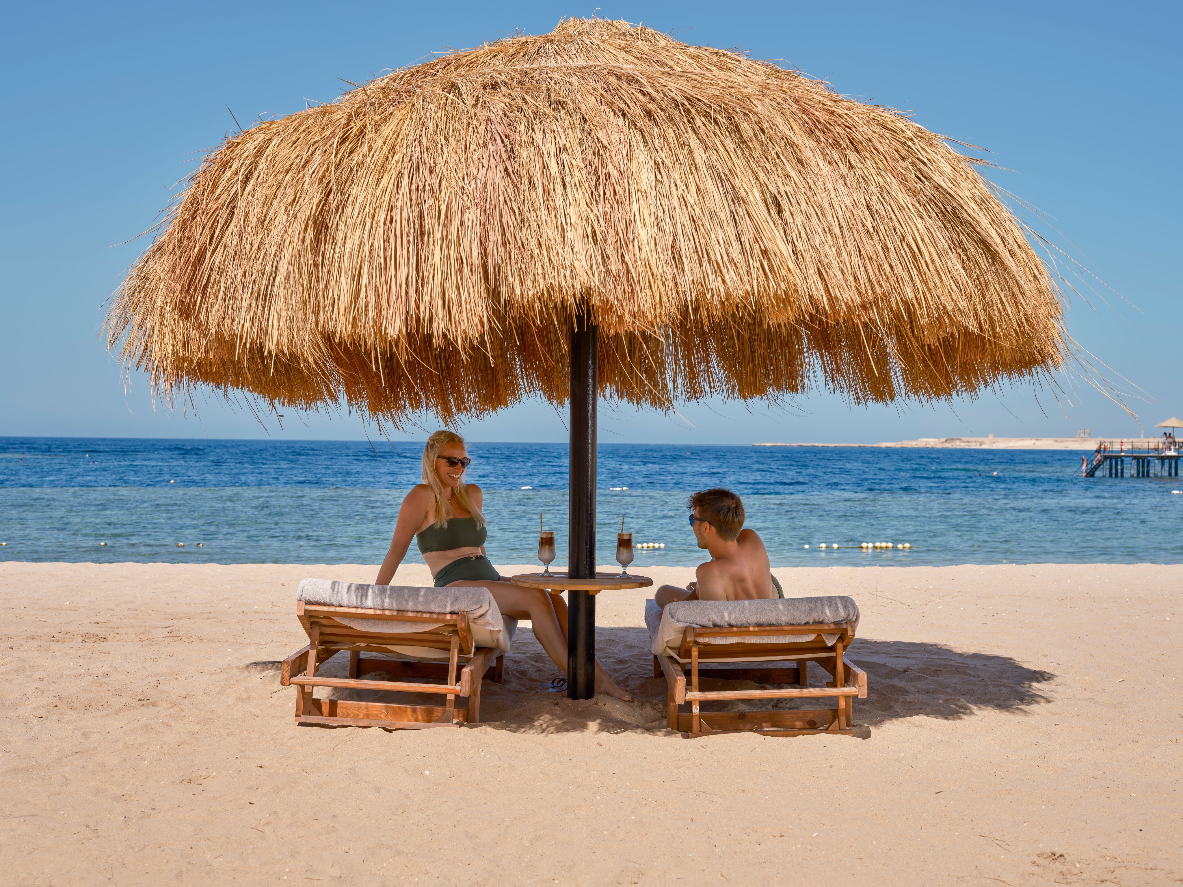 Ein Paar entspannt sich unter einem Strandsonnenschirm am Meer bei Aldiana Urlaub