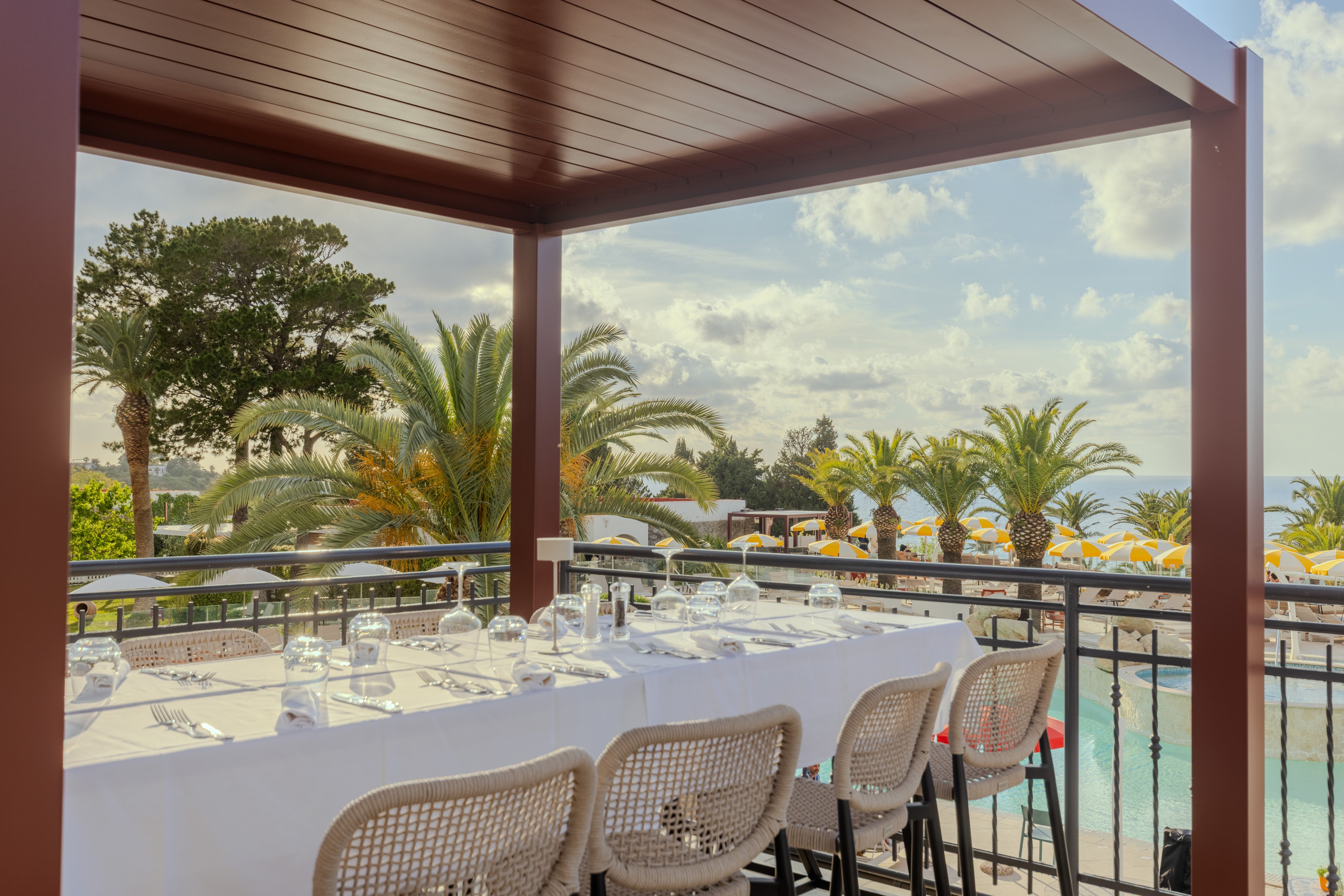Eleganter Außenbereich mit Tafel, Bänken und Blick auf Palmen und Pool bei Aldiana