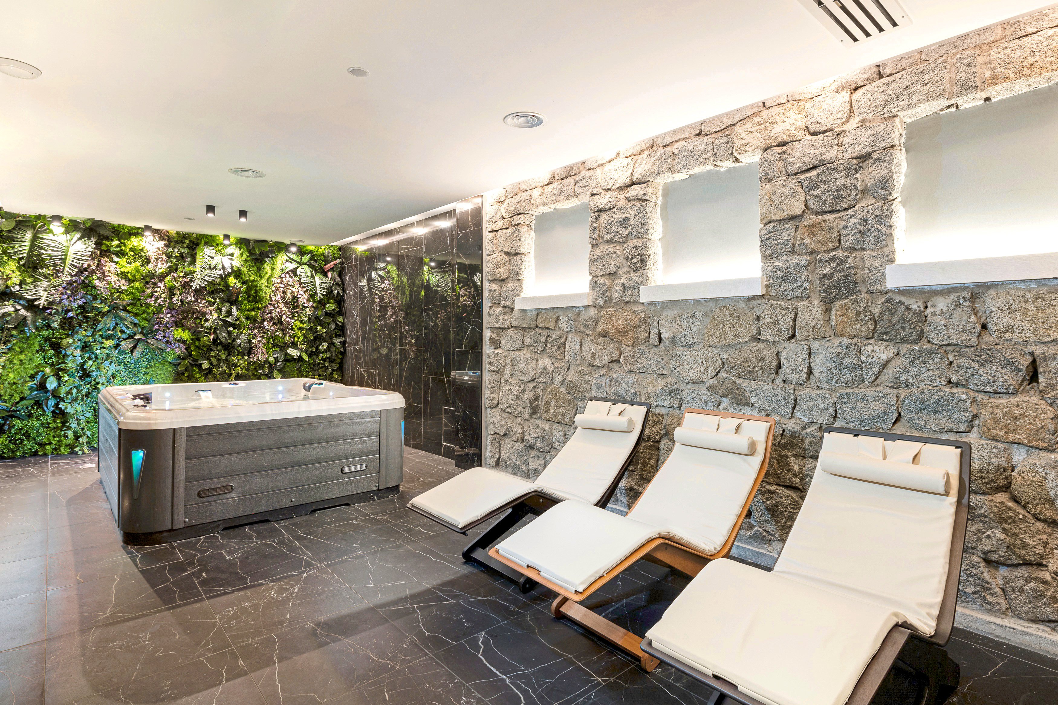 Wellnessbereich mit Whirlpool, Sonnenliegen und Natursteinwand im Hotel Aldiana.