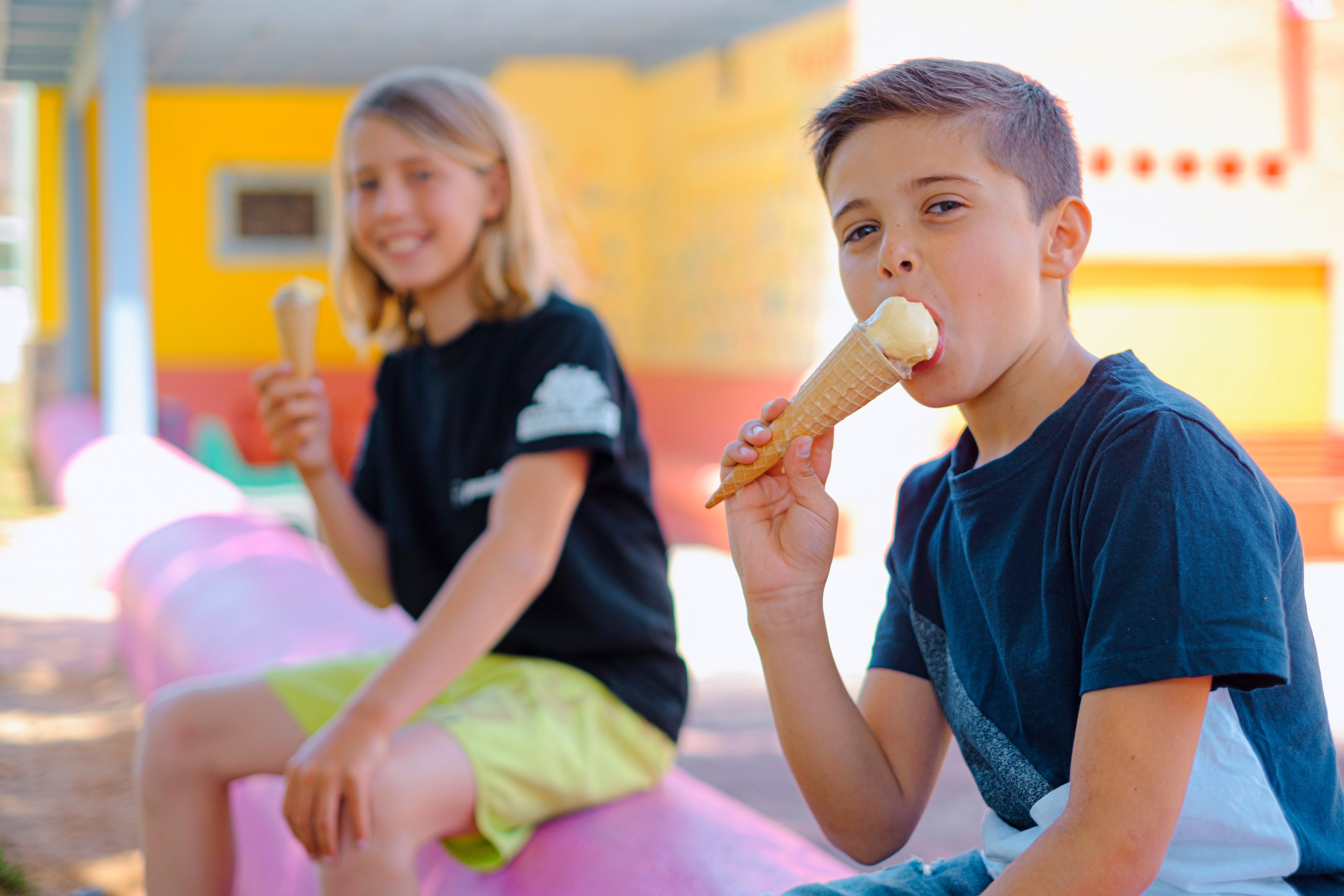 Zwei Kinder sitzen im Freizeitpark, genießen Eis und entspannen in der Sonne