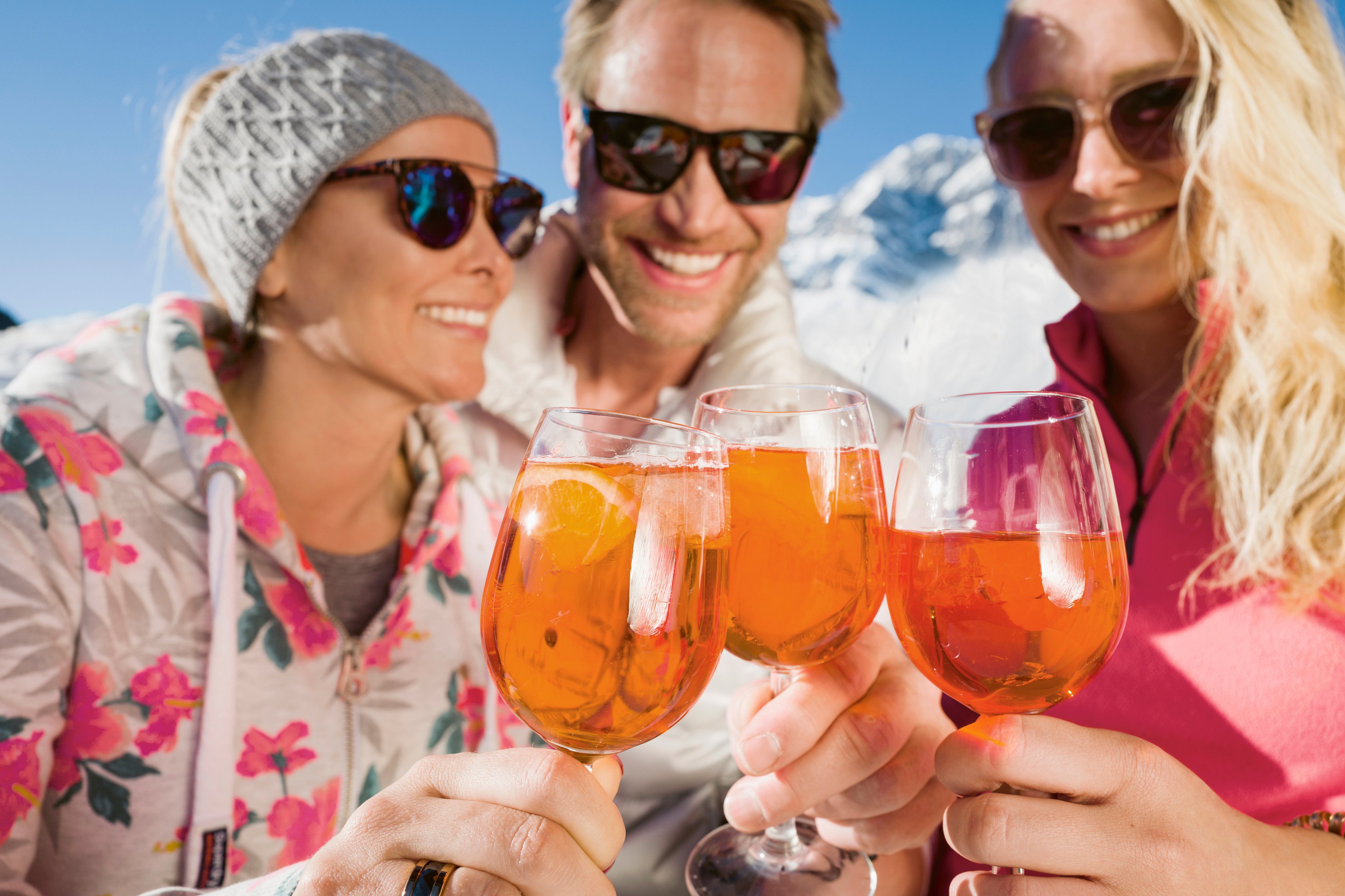 Drei Personen beim Prost trinken mit Aperol Spritz im sonnigen Urlaubsambiente