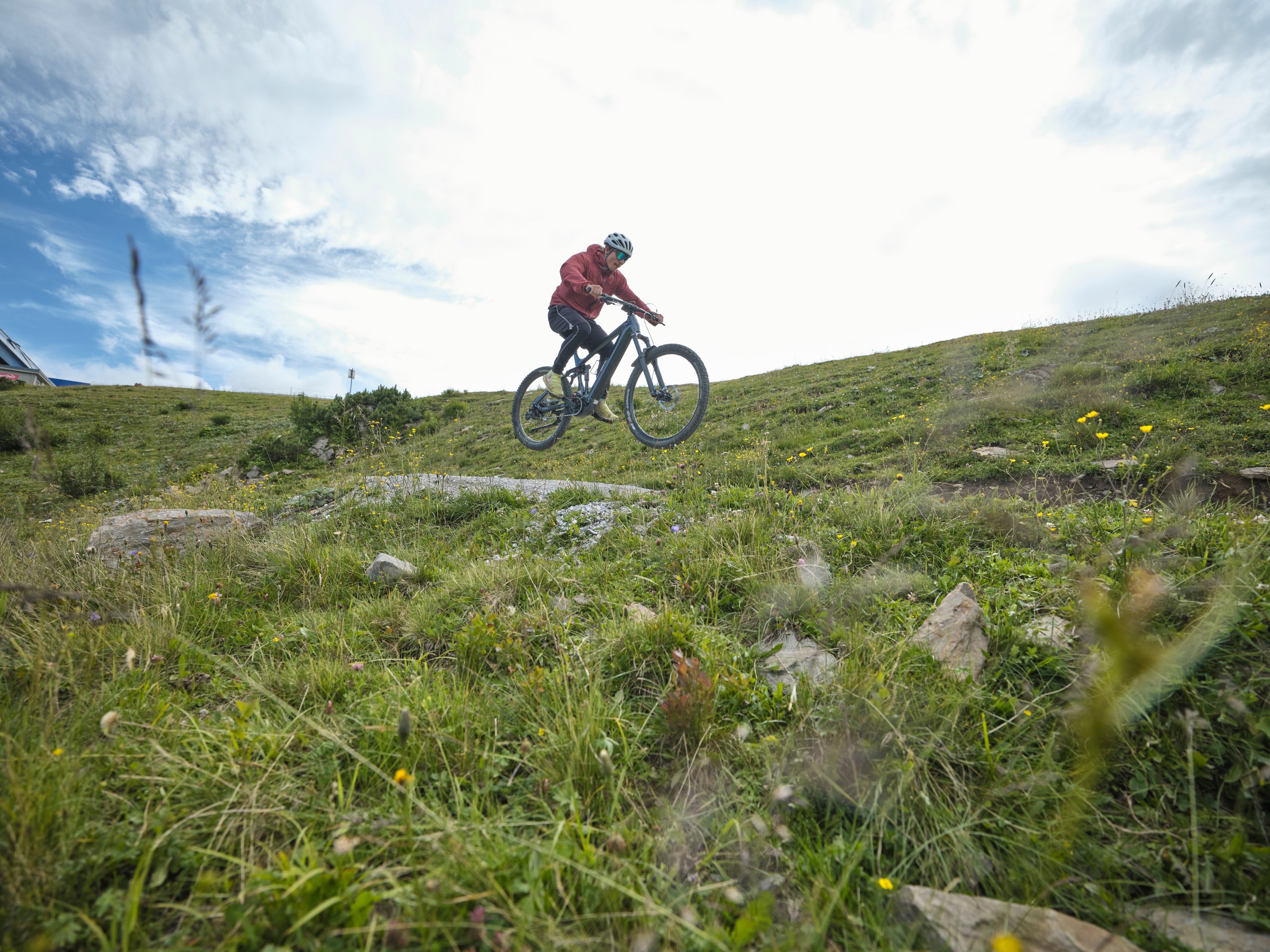 Person beim Mountainbiken auf grünem Hügel mit Himmel im Hintergrund