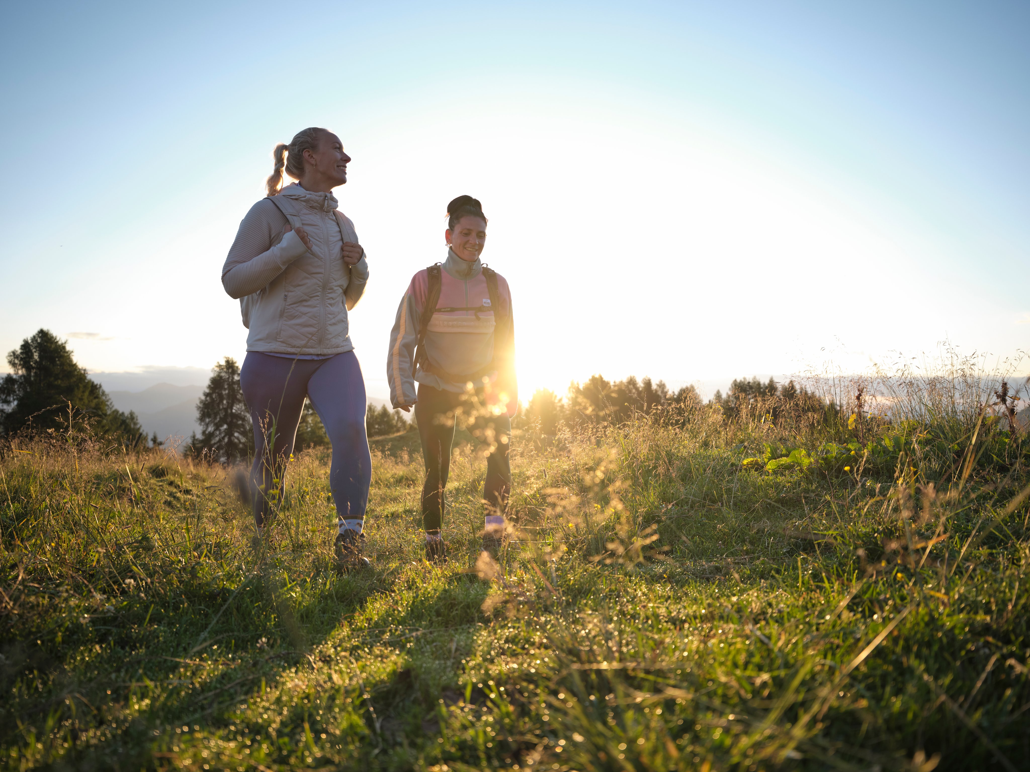 Zwei Frauen beim Wandern auf einer Wiese bei Sonnenaufgang, genießen einen Premium Urlaubsauftenthalt