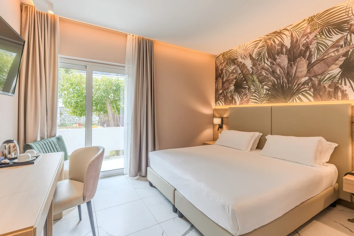 Ein stilvolles Hotelzimmer bei Aldiana mit Doppelbett, Sofa, Balkon und Pflanzenmotivwand