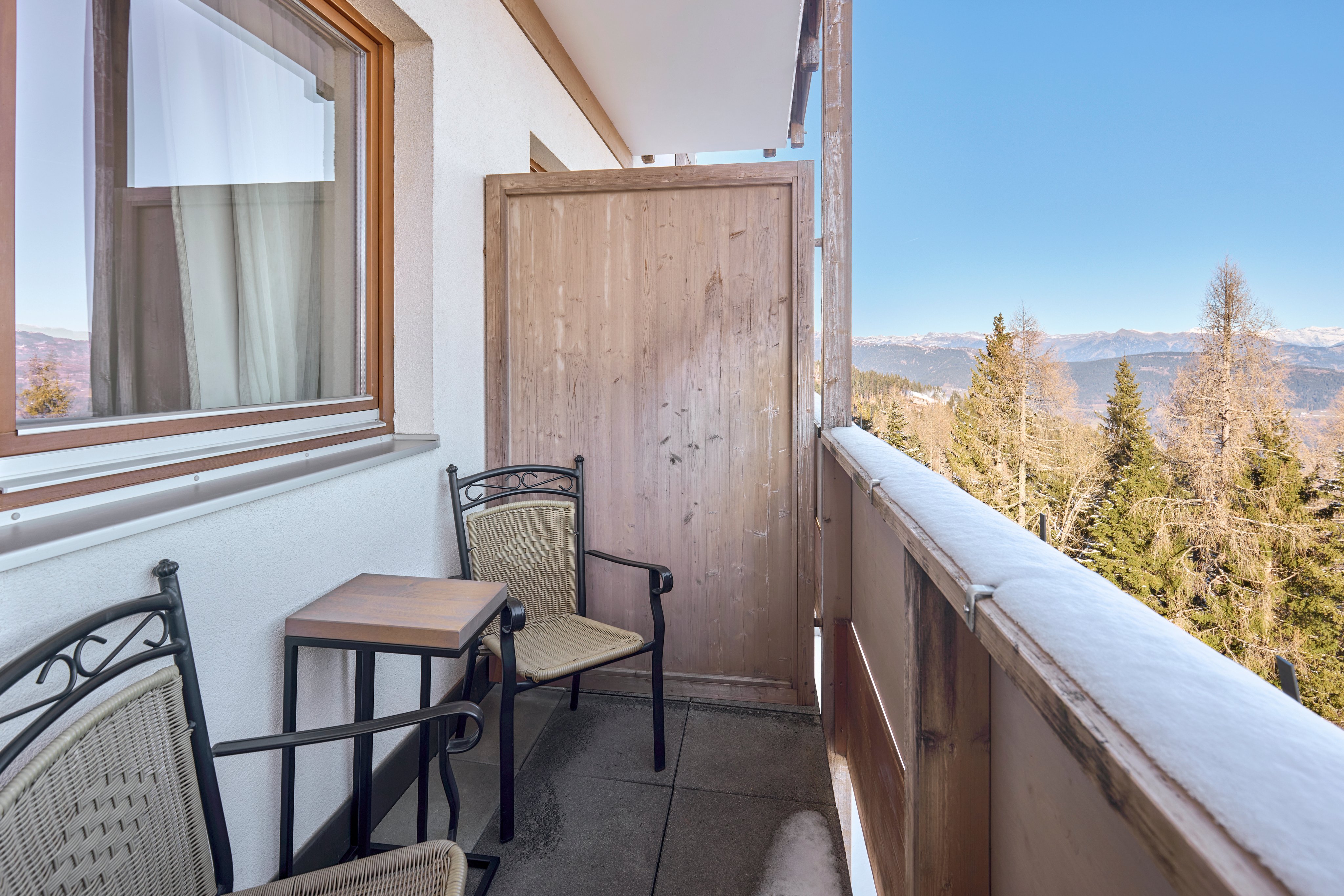 Balkon mit Sitzgelegenheit und Blick auf Wald und Berge bei Sonnenlicht