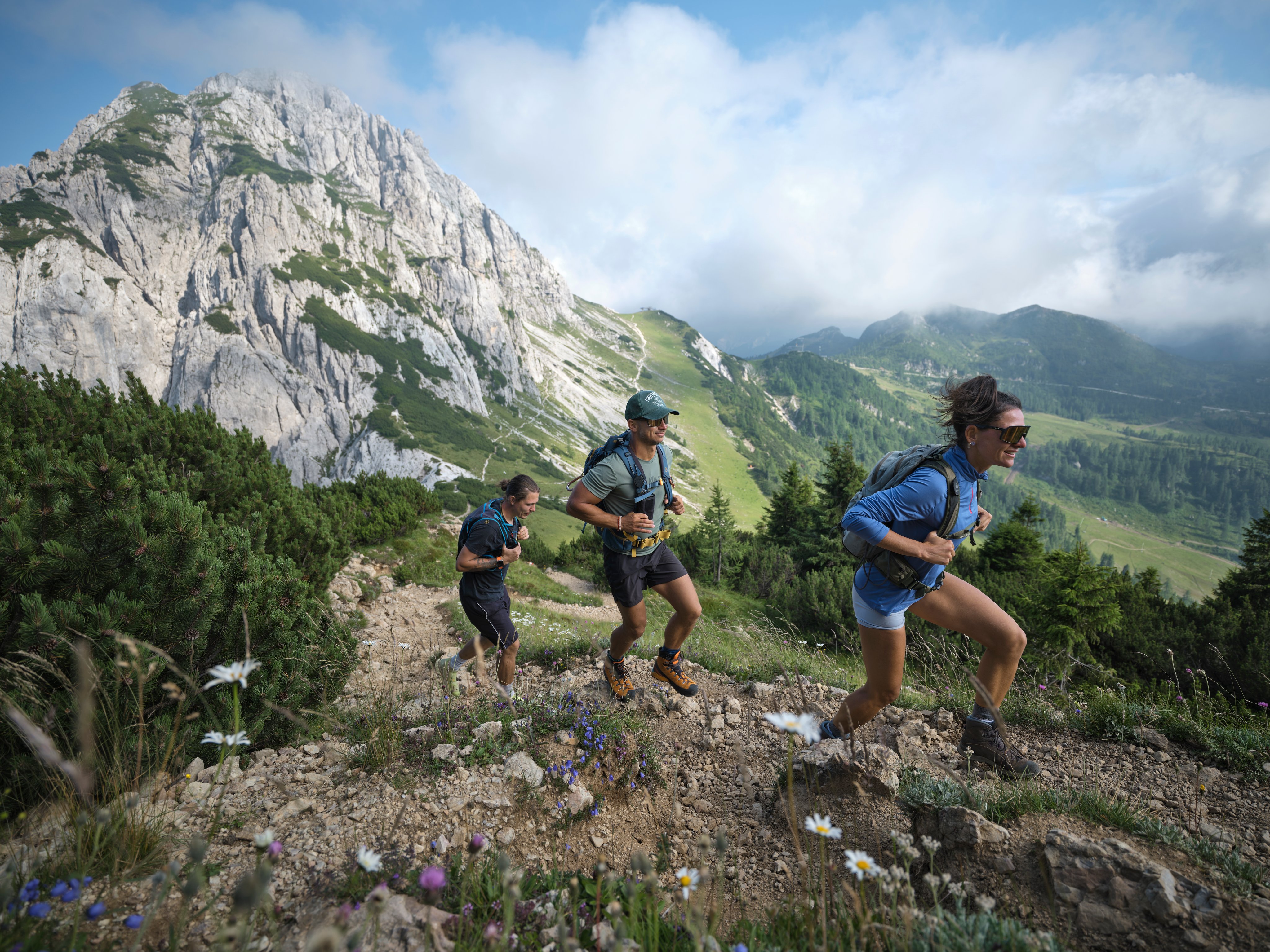 Drei Wanderer auf Bergpfad mit Blick auf grüne Berge und Himmel im Hintergrund